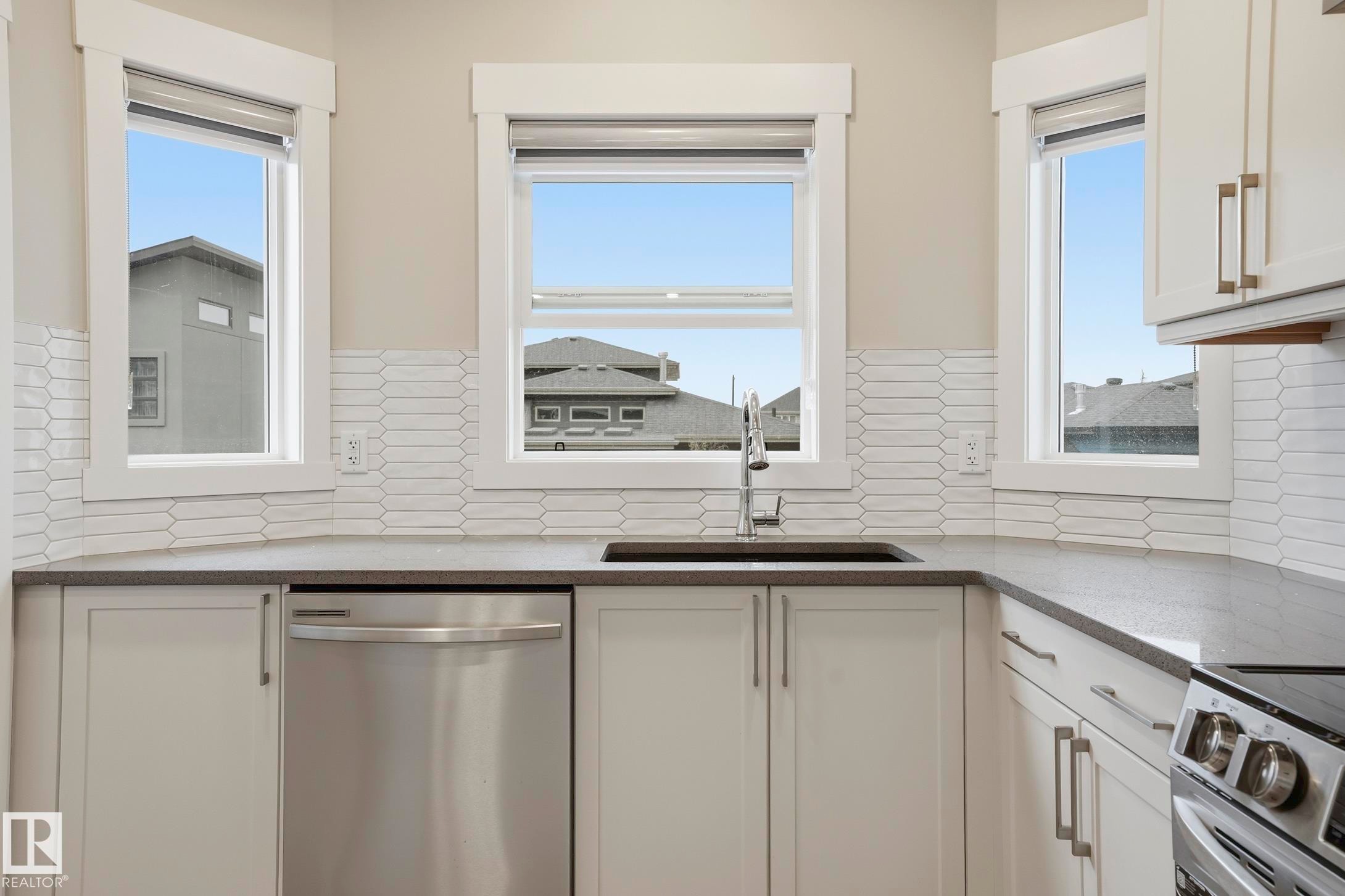 Kitchen featuring white cabinetry, dark countertops, and a full tile backsplash - 36 150 Everitt Dr, St. Albert, AB - Indoor Photo Showing Kitchen