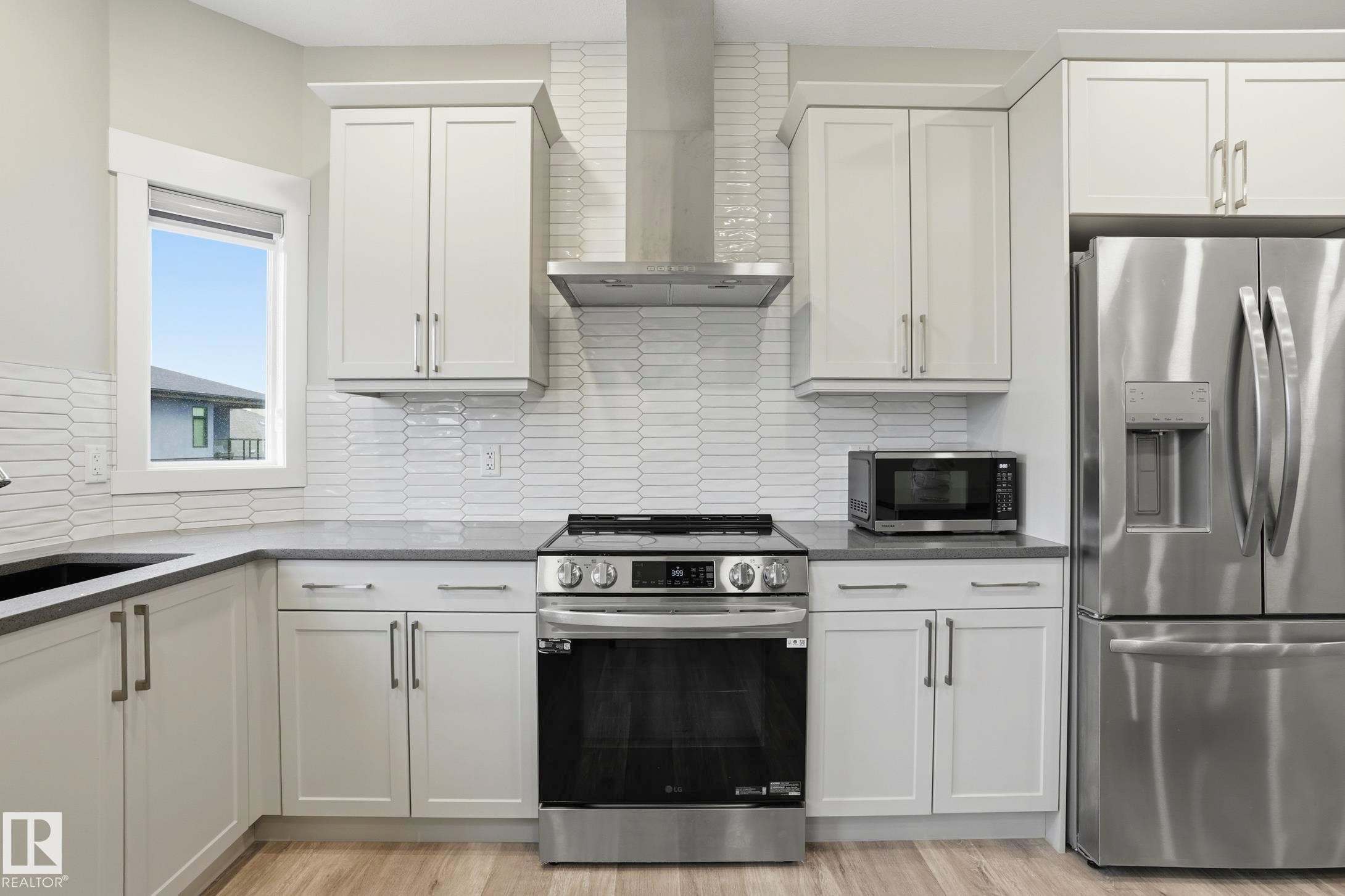 Modern kitchen featuring white shaker-style cabinetry, stainless steel appliances, a grey countertop, and a white picket tile backsplash - 36 150 Everitt Dr, St. Albert, AB - Indoor Photo Showing Kitchen With Stainless Steel Kitchen With Upgraded Kitchen