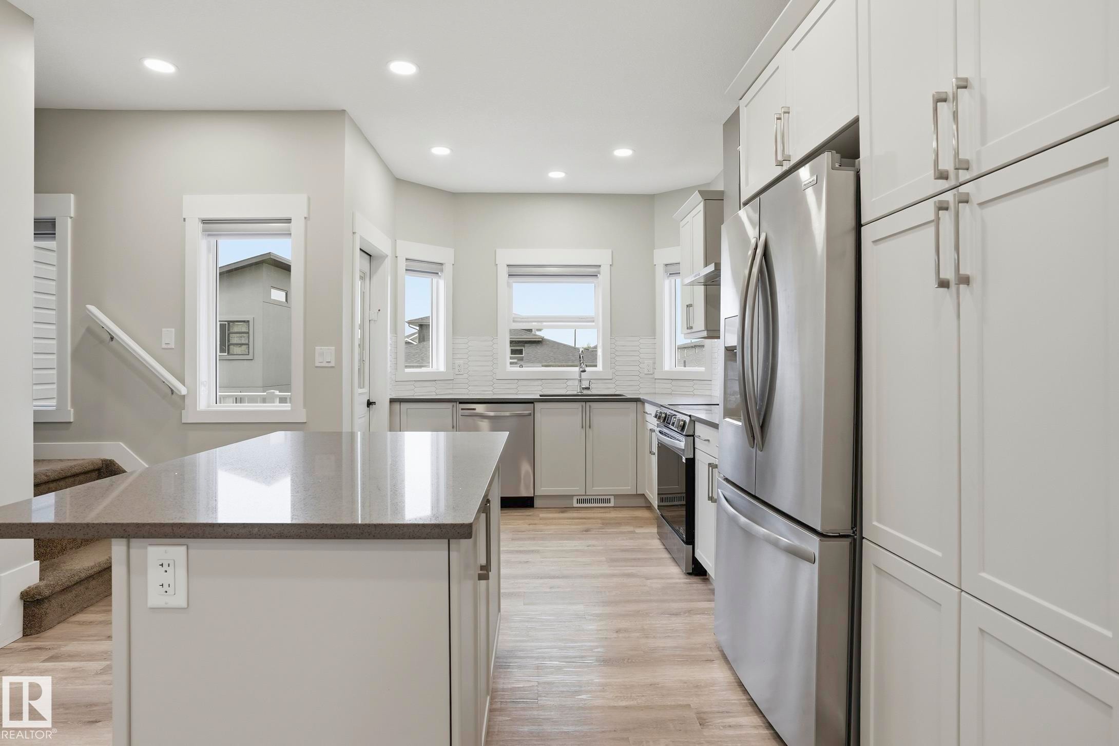 Modern kitchen featuring a central island with a stone-finish countertop, light-toned cabinetry, stainless steel appliances, and wood-finish flooring - 36 150 Everitt Dr, St. Albert, AB - Indoor Photo Showing Kitchen With Upgraded Kitchen