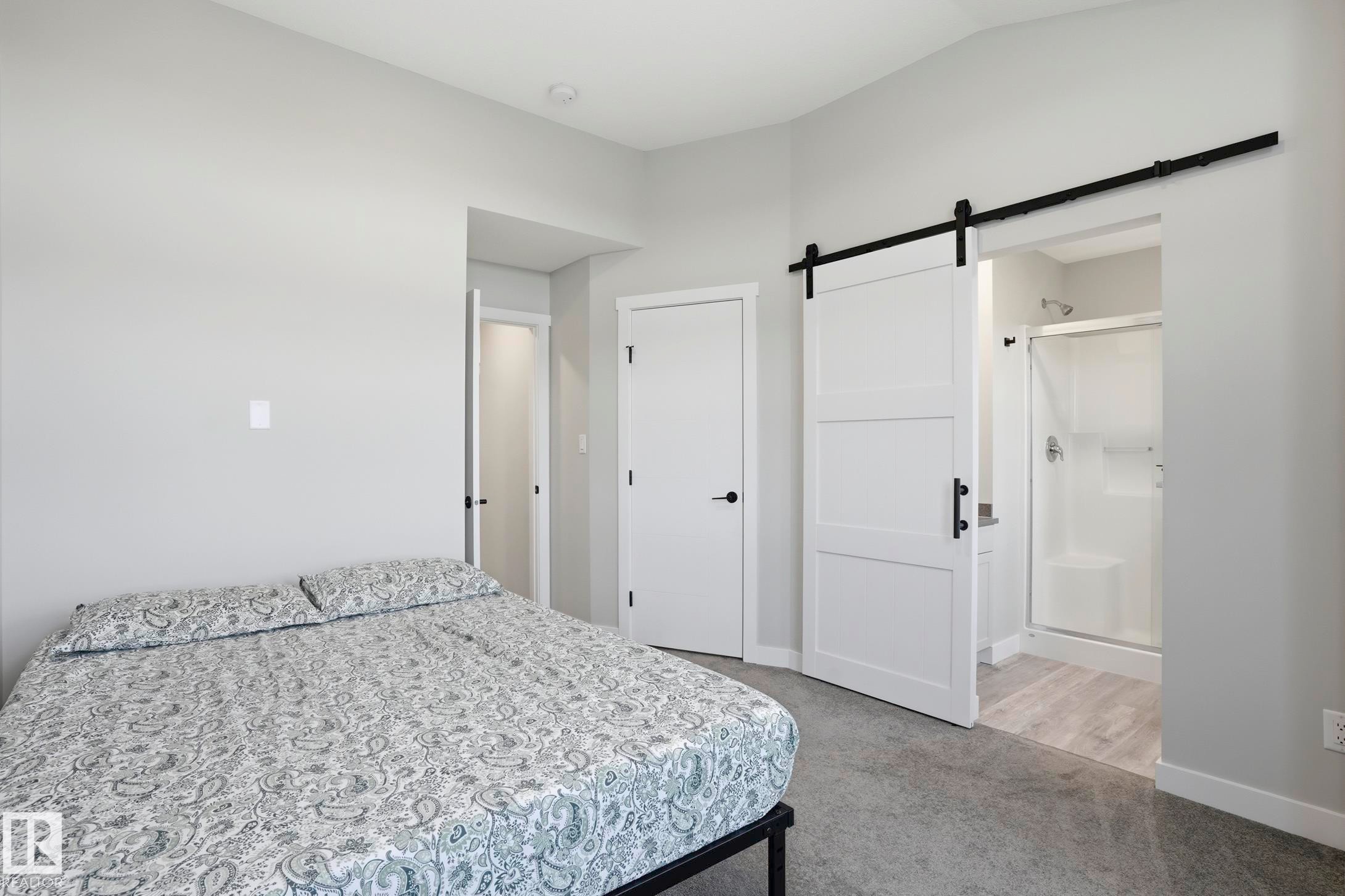 Bedroom featuring light gray walls, gray carpeting, and a white barn door leading to an attached bathroom - 36 150 Everitt Dr, St. Albert, AB - Indoor Photo Showing Bedroom
