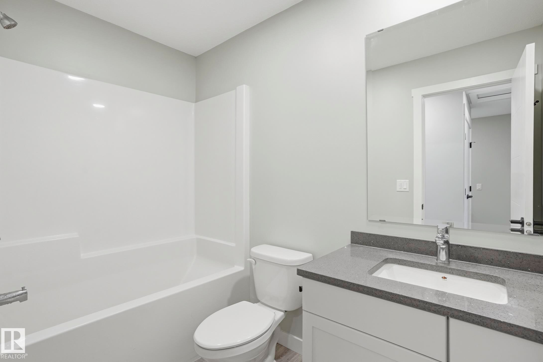 Bathroom featuring a built-in tub/shower combination, a vanity with a dark countertop, a rectangular undermount sink, and a wall-mounted mirror - 36 150 Everitt Dr, St. Albert, AB - Indoor Photo Showing Bathroom