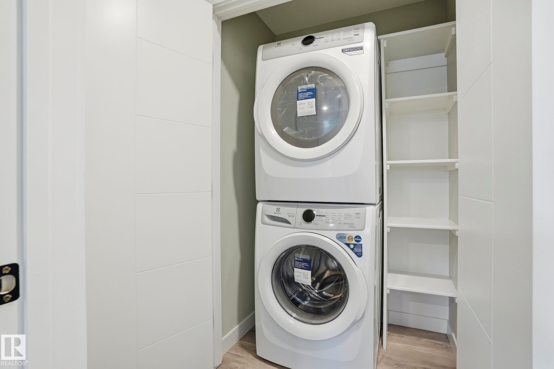 Laundry closet featuring a stacked washer and dryer, built-in shelving, and light wood-finish flooring - 36 150 Everitt Dr, St. Albert, AB - Indoor Photo Showing Laundry Room