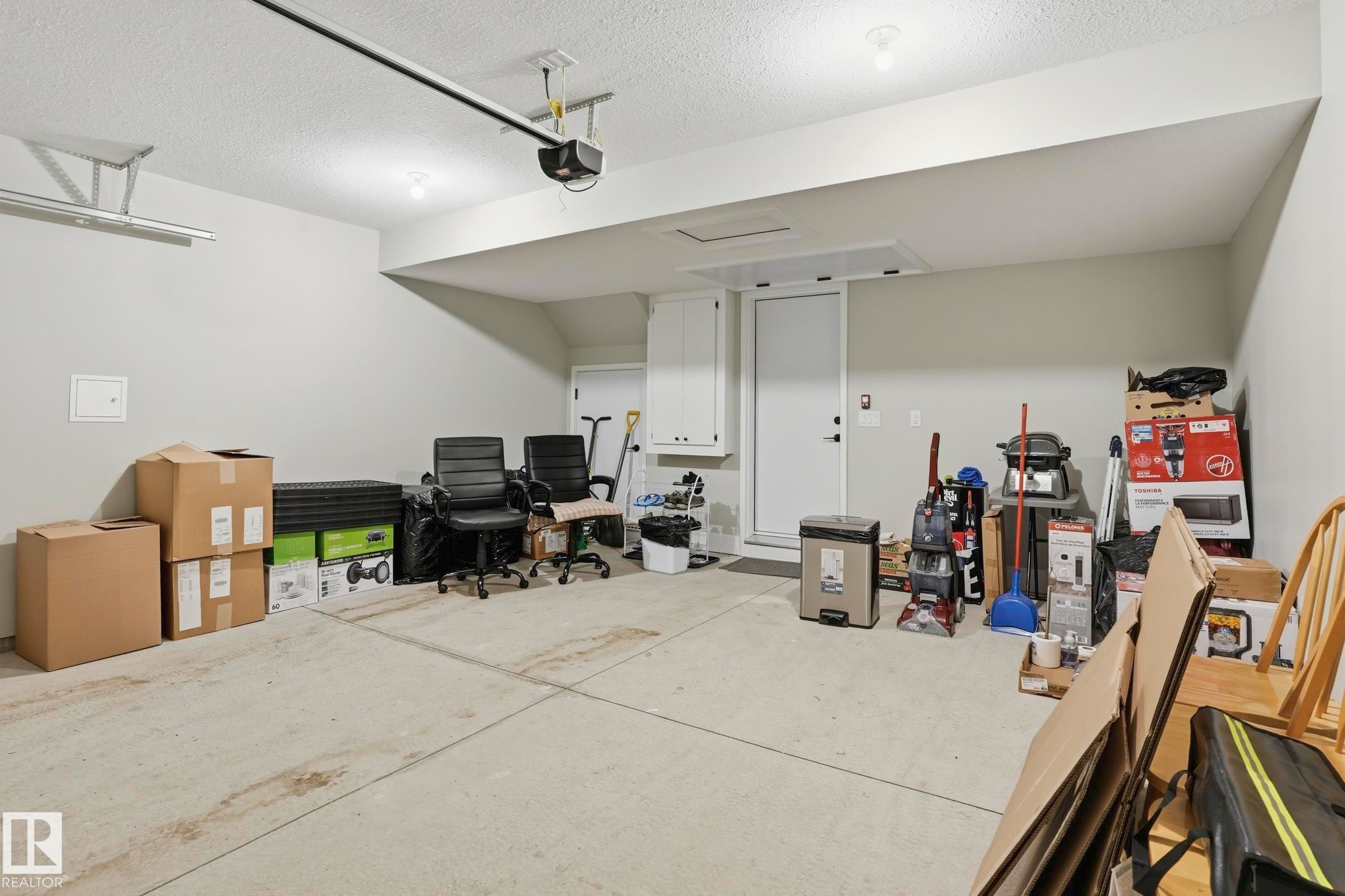 Spacious garage featuring a light gray painted interior, concrete flooring, overhead lighting, and an automatic garage door opener system - 36 150 Everitt Dr, St. Albert, AB - Indoor
