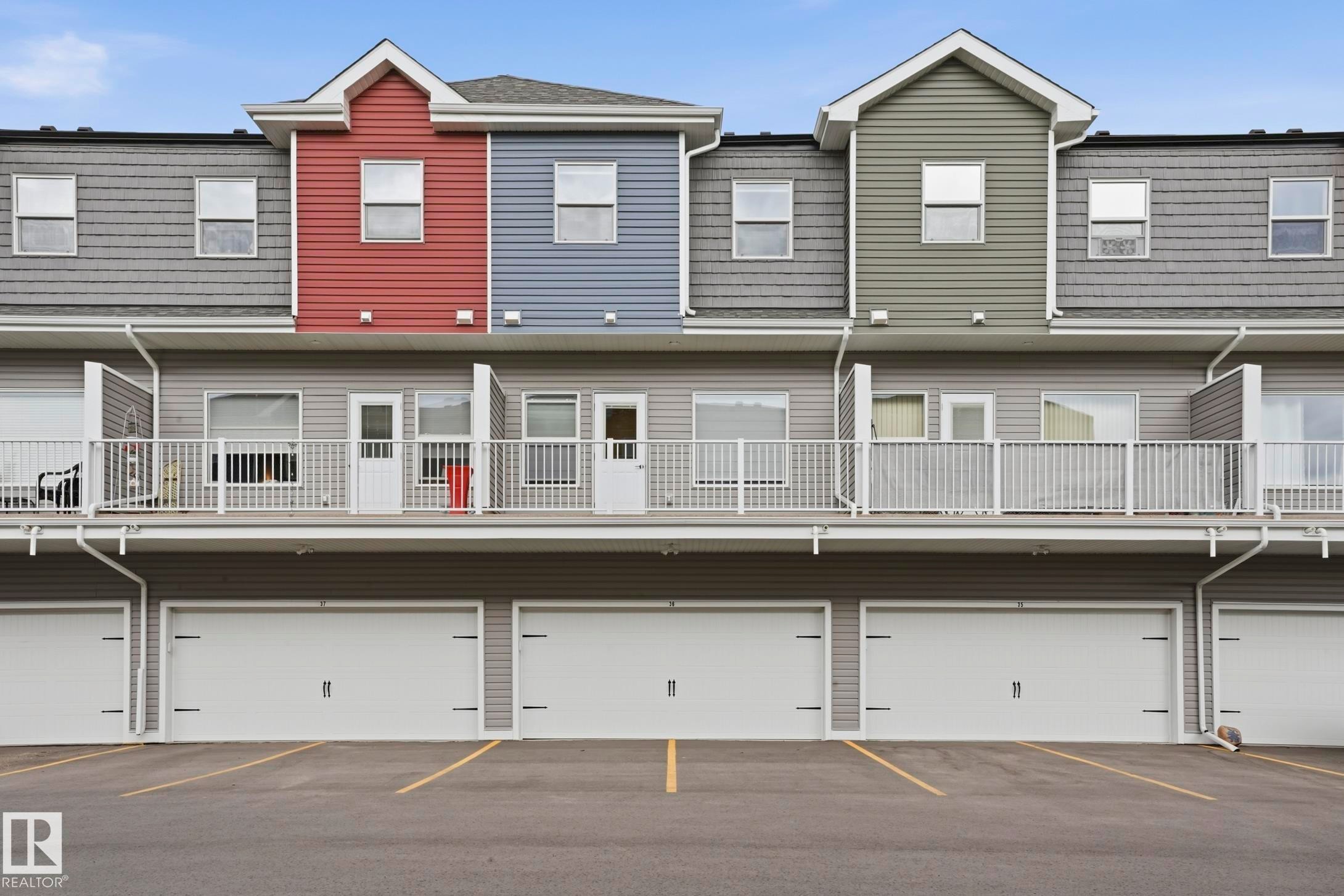 Townhome exterior featuring individual garage doors, second-level balconies with white railings, and multi-colored siding accents - 36 150 Everitt Dr, St. Albert, AB - Outdoor With Balcony