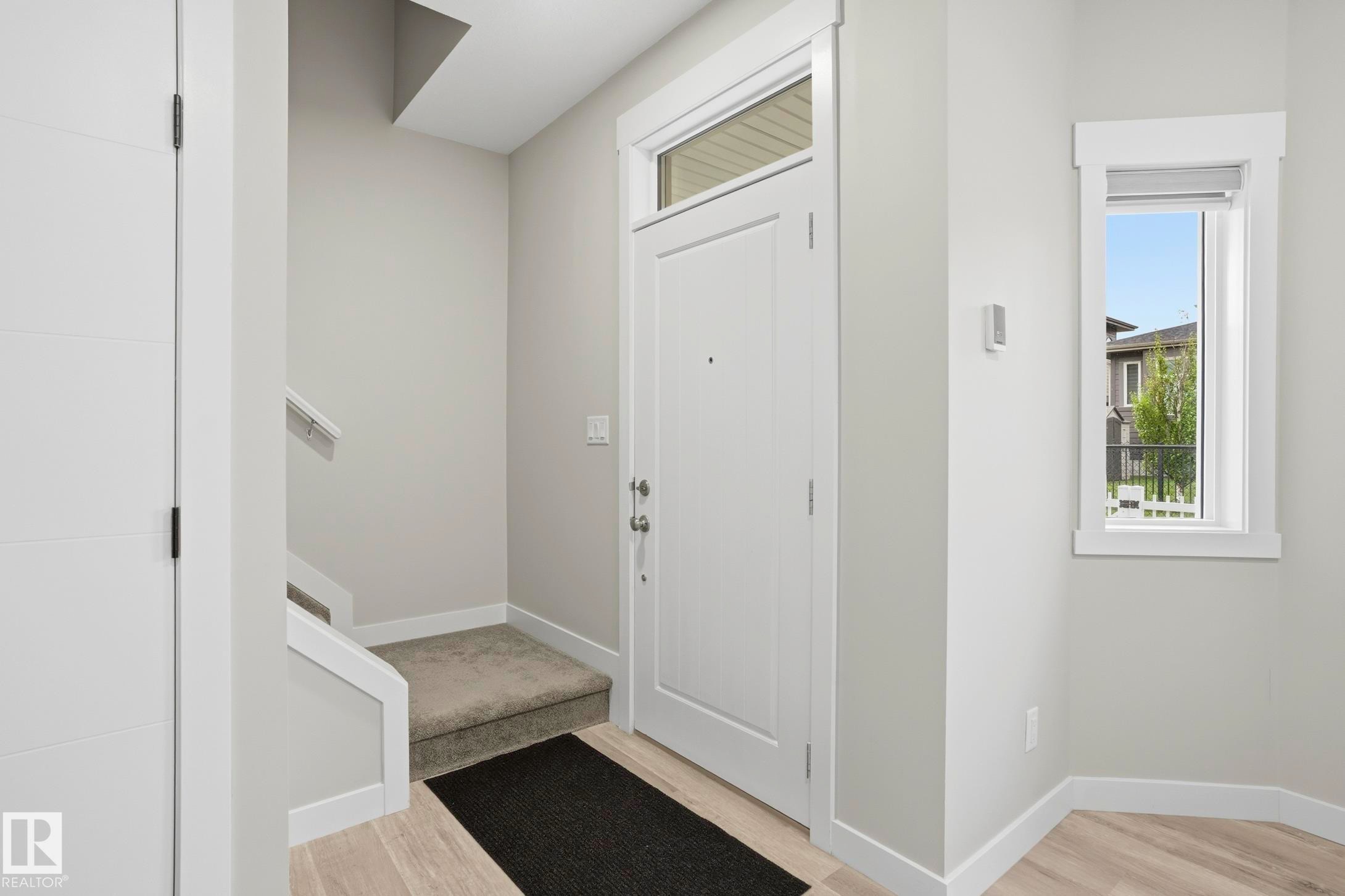 Entryway featuring a white paneled door with transom window, light wood-finish flooring, a small window, and a carpeted stairwell - 36 150 Everitt Dr, St. Albert, AB - Indoor Photo Showing Other Room
