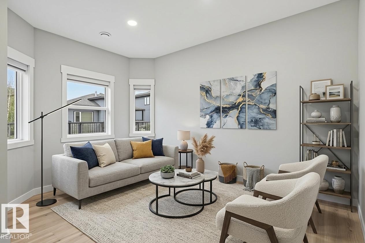 Living area featuring light wood-finish flooring, multiple windows with white trim, recessed lighting, and a built-in shelving unit with dark metal framing and wood-finish shelves - 36 150 Everitt Dr, St. Albert, AB - Indoor Photo Showing Living Room