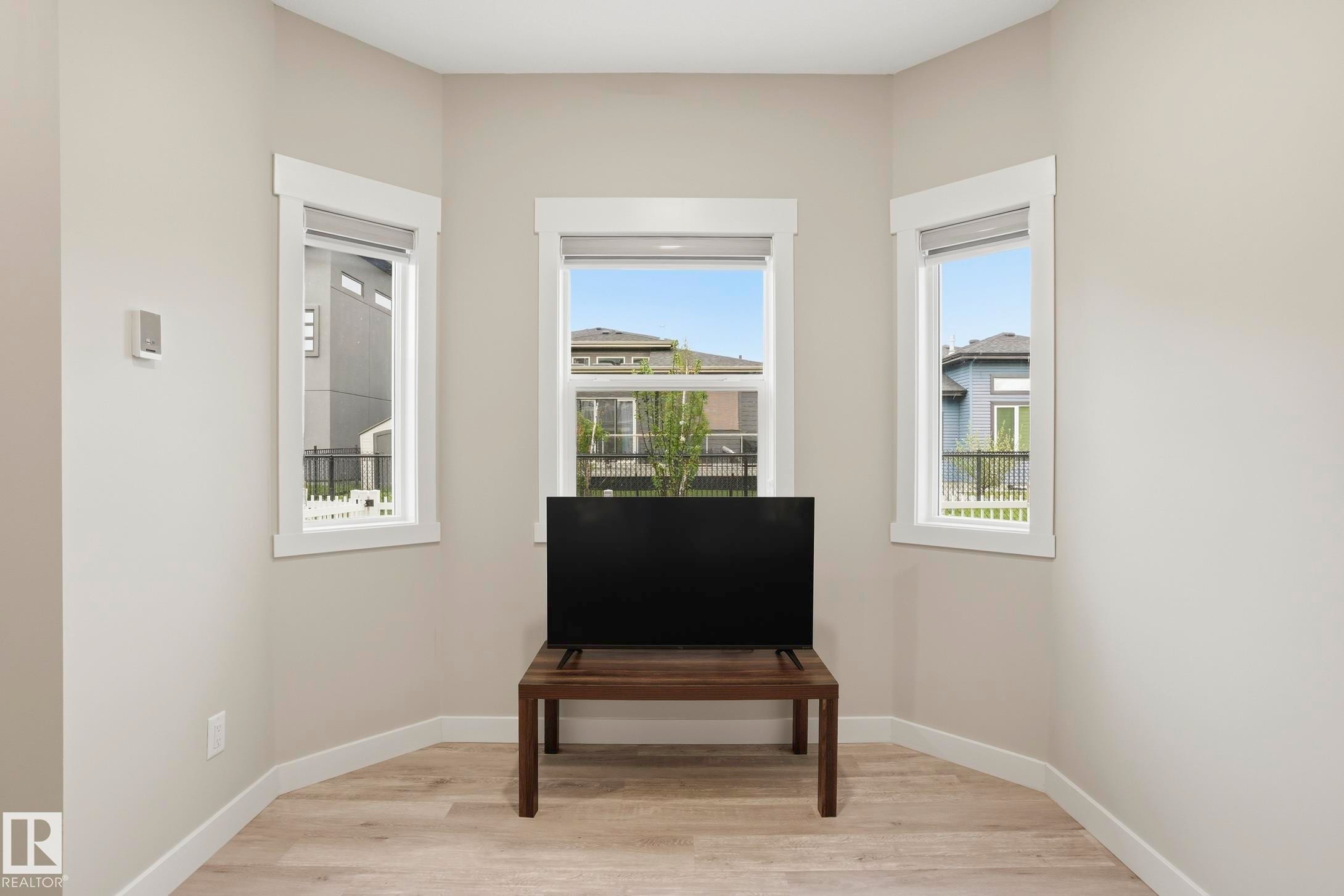 Corner room featuring three windows with white trim, light tone walls, and wood-finish flooring - 36 150 Everitt Dr, St. Albert, AB - Indoor Photo Showing Other Room