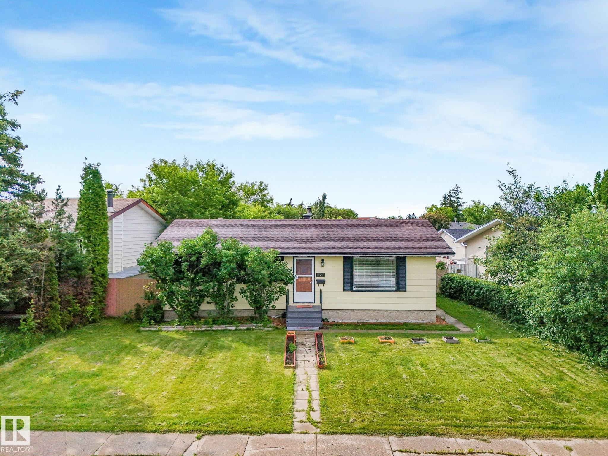 Single-story residence featuring a light yellow exterior and a dark brown shingle roof - 9315 151 Avenue, Edmonton, AB
