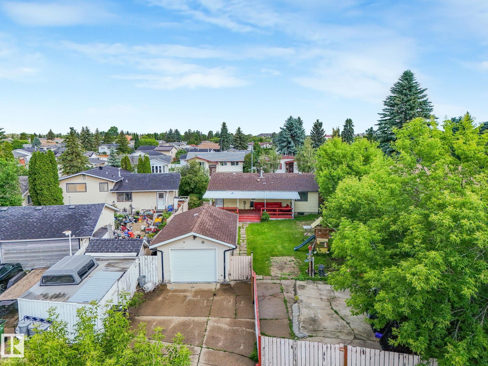 Rear property view featuring a detached garage with a white overhead door, a paved driveway, and a fenced yard with mature trees - 9315 151 Avenue, Edmonton, AB