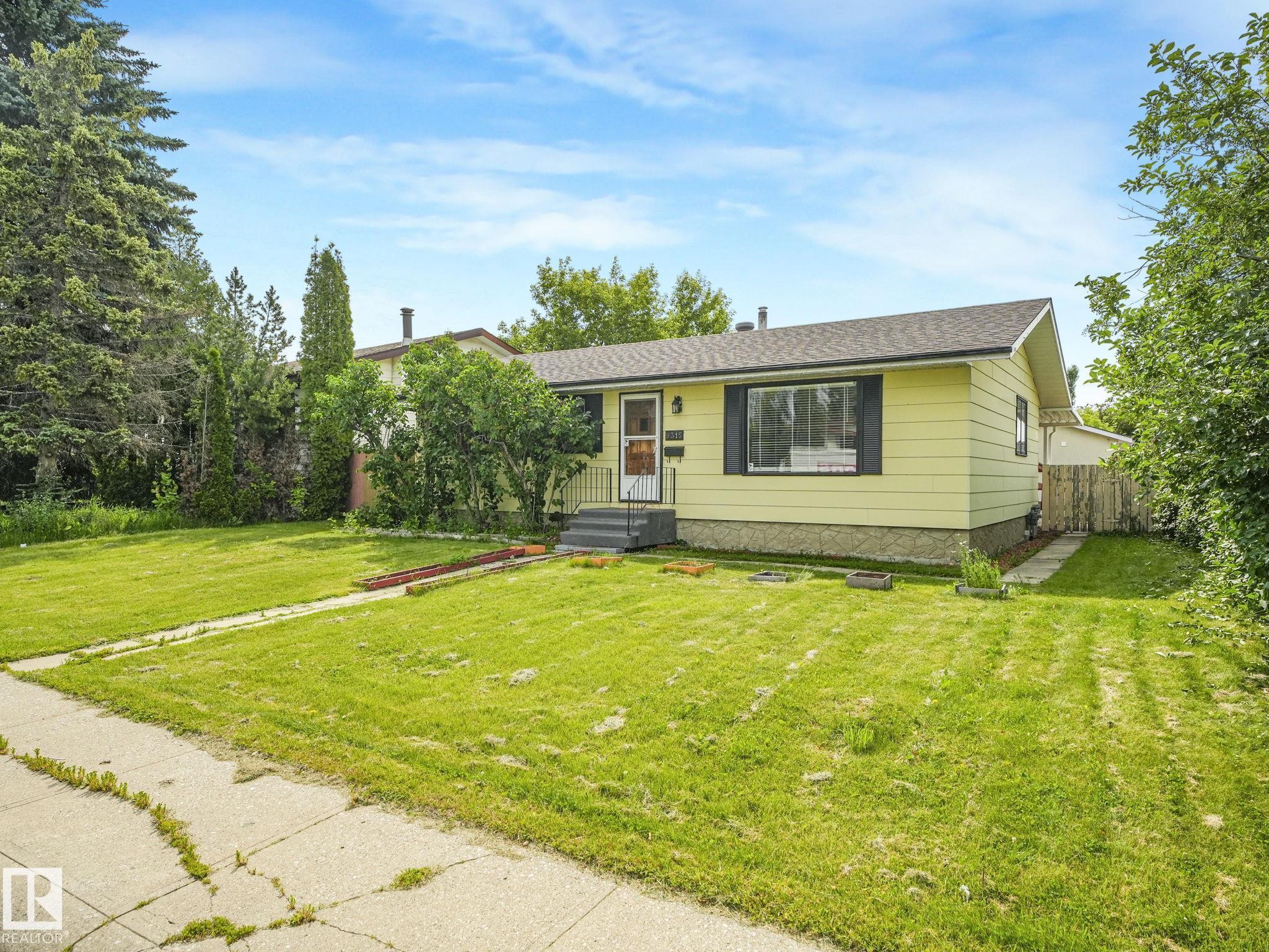 Single-story residence featuring light yellow siding, a dark shingle roof, and a front entry porch with steps - 9315 151 Avenue, Edmonton, AB