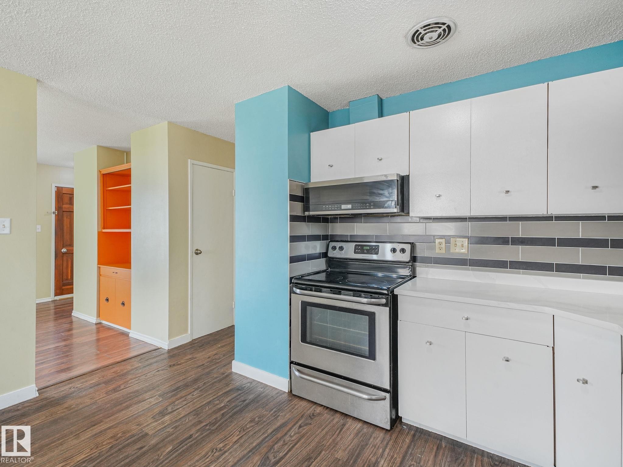 Kitchen featuring stainless steel range and microwave, white cabinetry, light-toned countertops, and a gray-tiled backsplash - 9315 151 Avenue, Edmonton, AB