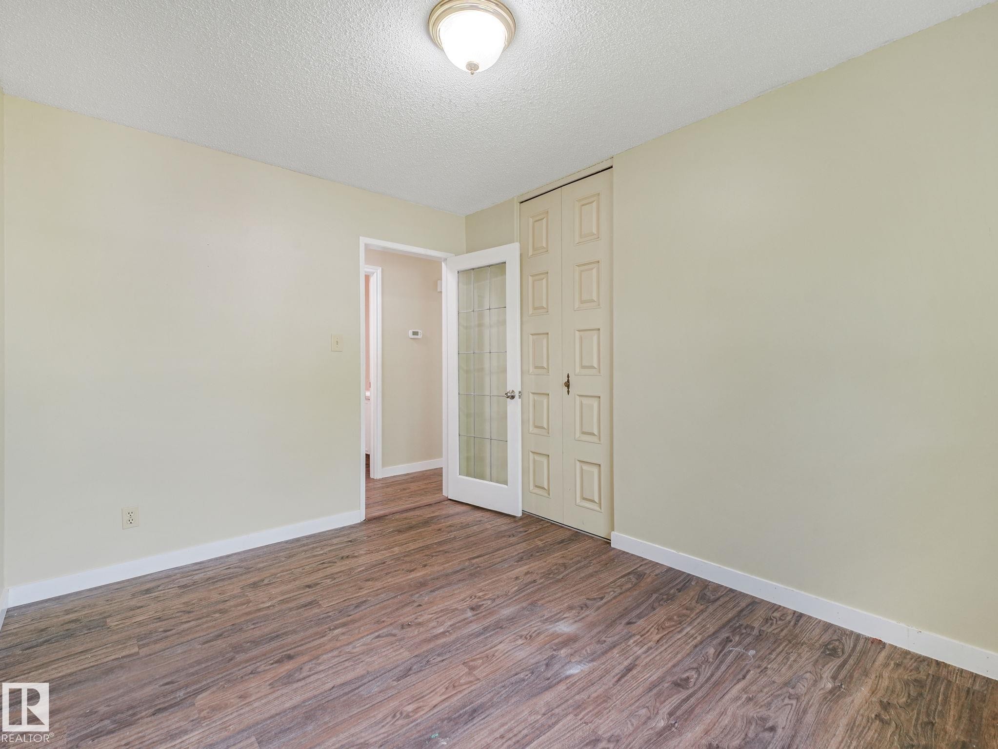 Spacious room featuring wood-finish flooring, light-toned walls, and a textured ceiling - 9315 151 Avenue, Edmonton, AB