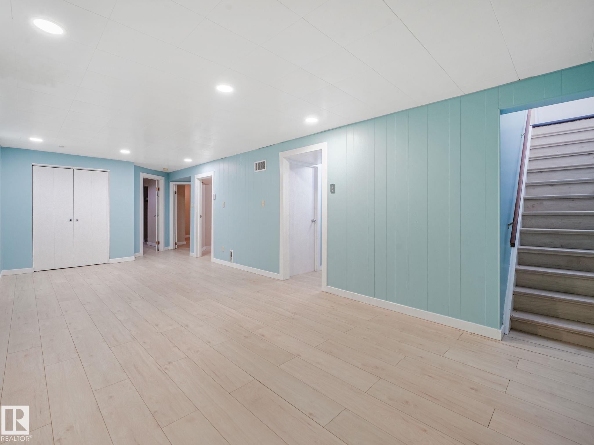 Spacious room featuring light wood-finish flooring, recessed lighting, and light blue vertical plank wall paneling - 9315 151 Avenue, Edmonton, AB