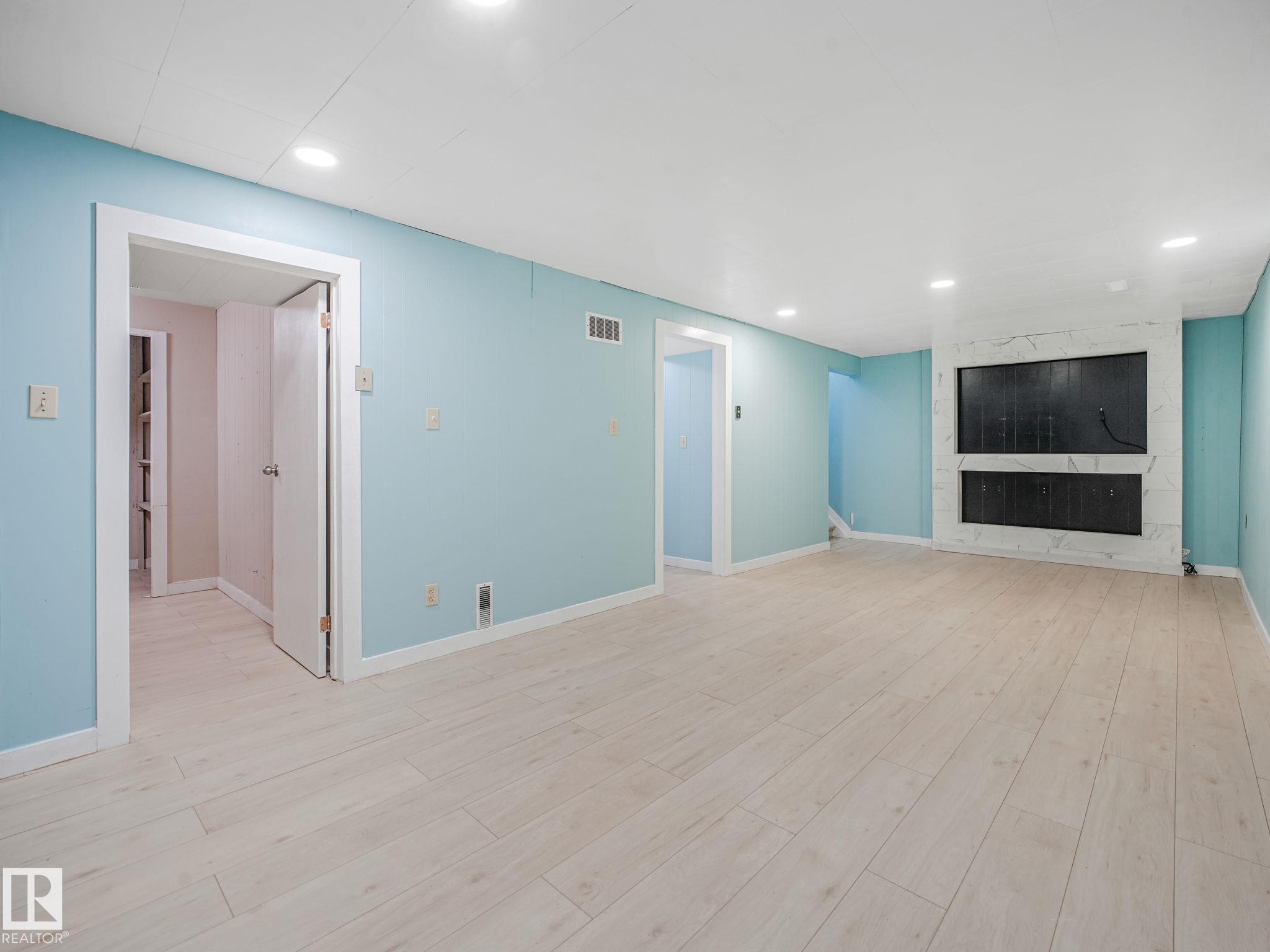 Spacious interior featuring light wood-finish flooring, recessed lighting, and a modern fireplace with a marble-look surround - 9315 151 Avenue, Edmonton, AB