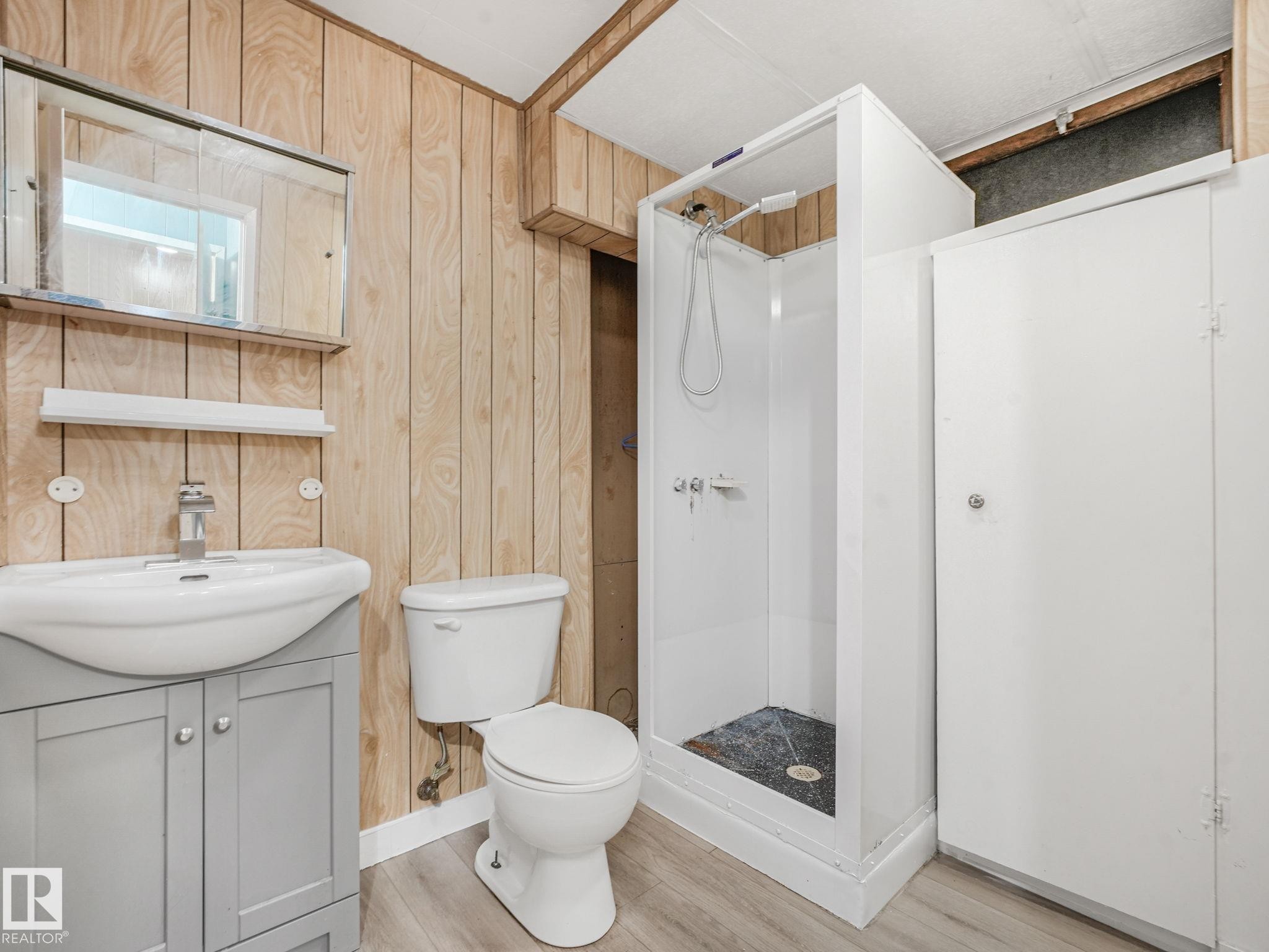 Bathroom featuring a white shower stall, wood-finish wall paneling, and a light gray vanity with a white countertop sink - 9315 151 Avenue, Edmonton, AB