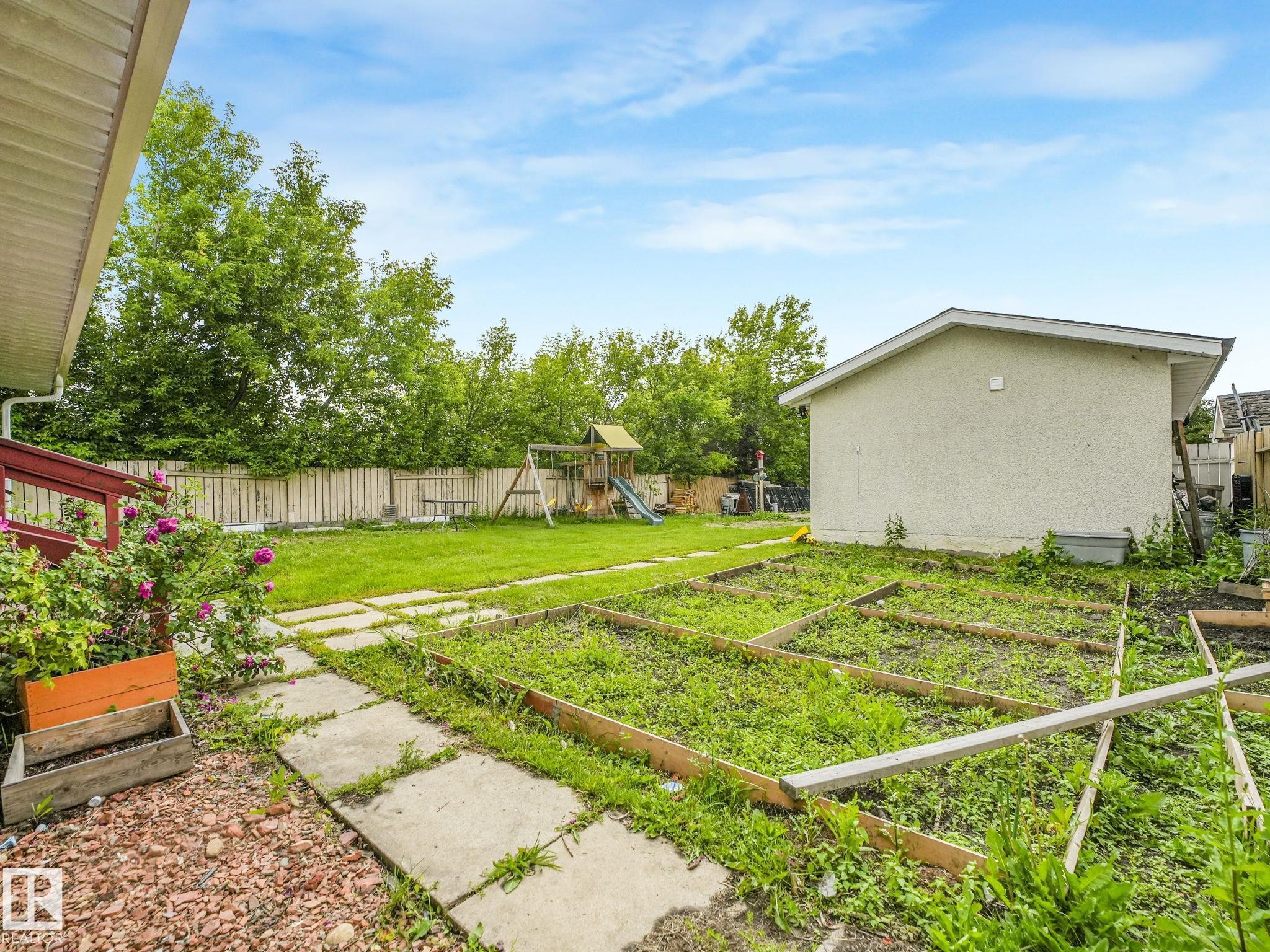 Expansive rear yard featuring a concrete paver pathway, multiple raised garden beds, a detached shed, and a wooden privacy fence - 9315 151 Avenue, Edmonton, AB