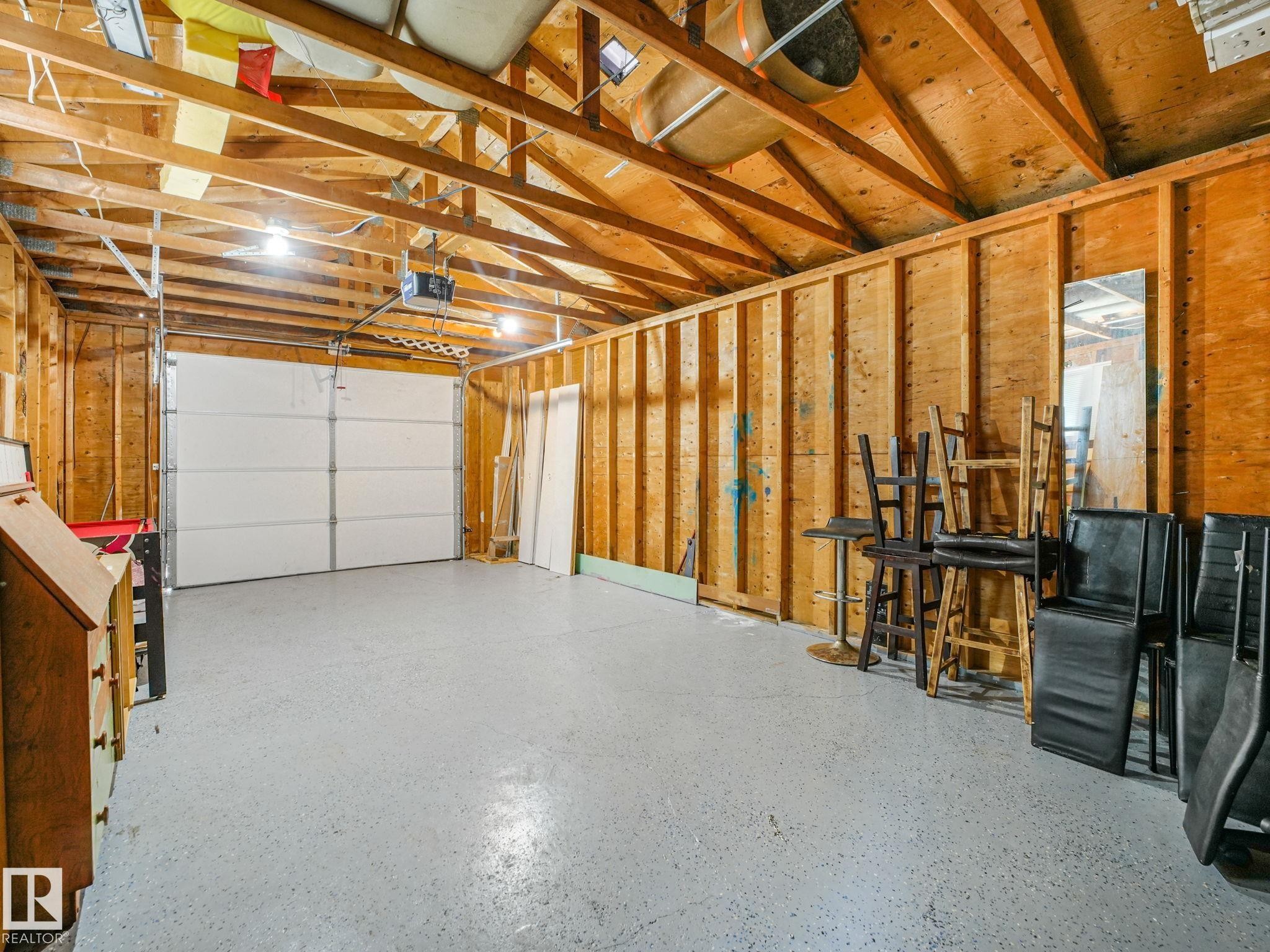 Spacious garage featuring exposed wood framing, an overhead garage door, and a light-colored epoxy floor coating - 9315 151 Avenue, Edmonton, AB