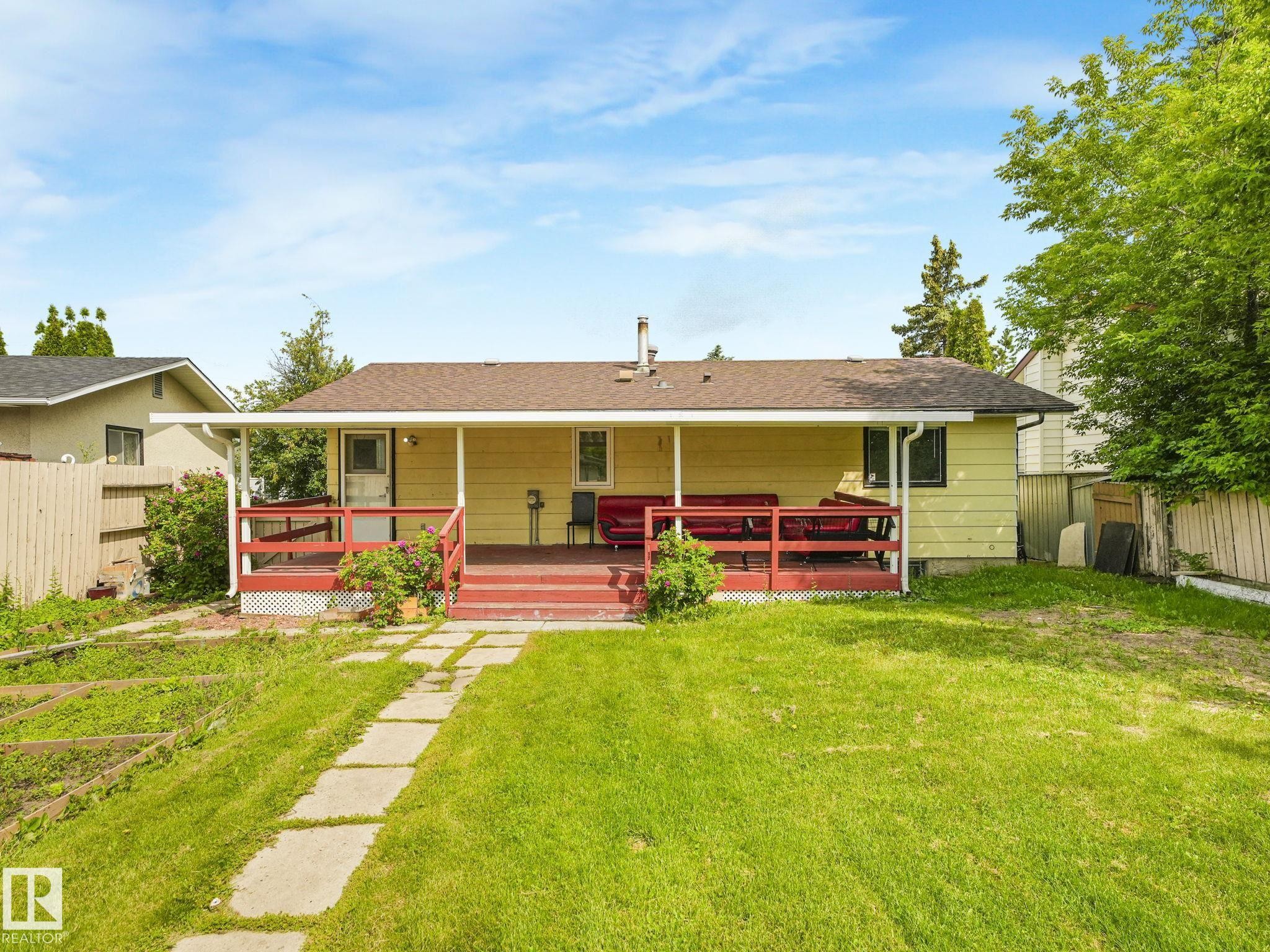 Rear exterior featuring an expansive covered deck, a spacious grassy lawn, and a stepping stone pathway - 9315 151 Avenue, Edmonton, AB
