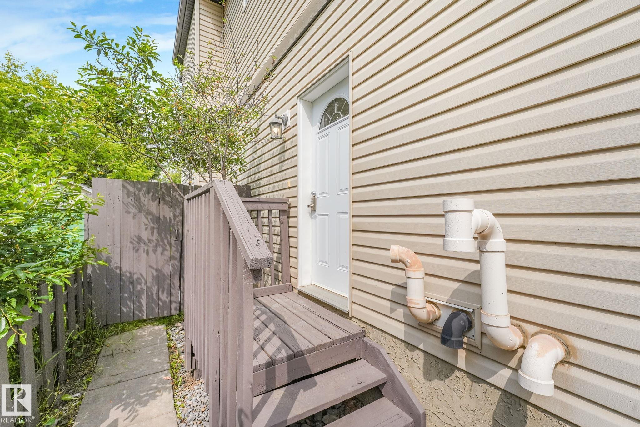 Side entrance featuring a privacy fence, exterior lighting, wood-finish steps, and a concrete pathway - 10216 150 Street Nw, Edmonton, AB - Outdoor