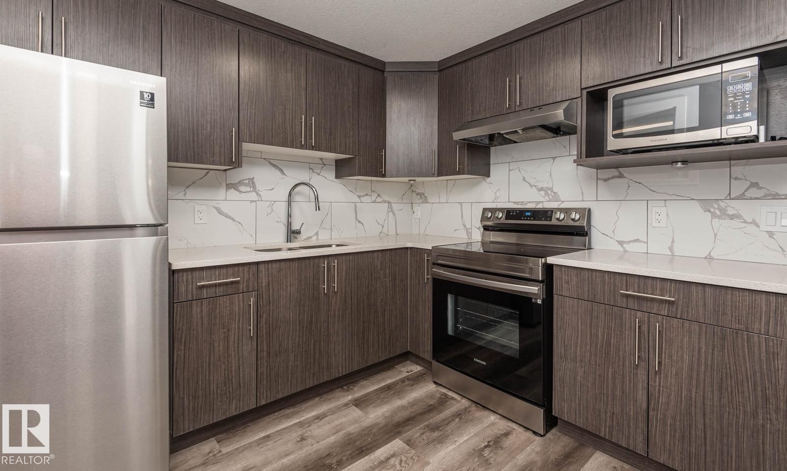 Contemporary kitchen featuring wood-finish cabinetry, stainless steel appliances, a white veined backsplash, light-toned countertops, and wood-look flooring - 2635 Donaghey Crescent, Edmonton, AB