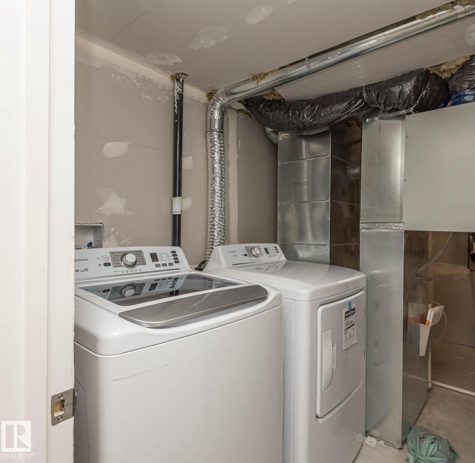 Dedicated laundry area featuring a white top-load washing machine and white dryer, with exposed ductwork and utility piping - 2635 Donaghey Crescent, Edmonton, AB