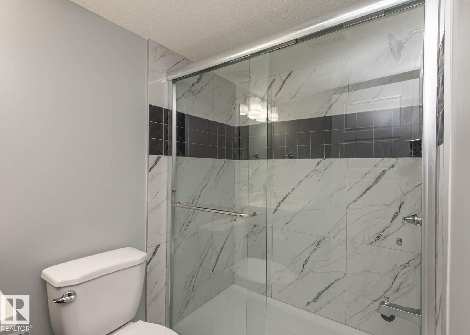 Shower enclosure featuring sliding glass doors, white marble-look tile, and a dark accent tile band - 2635 Donaghey Crescent, Edmonton, AB