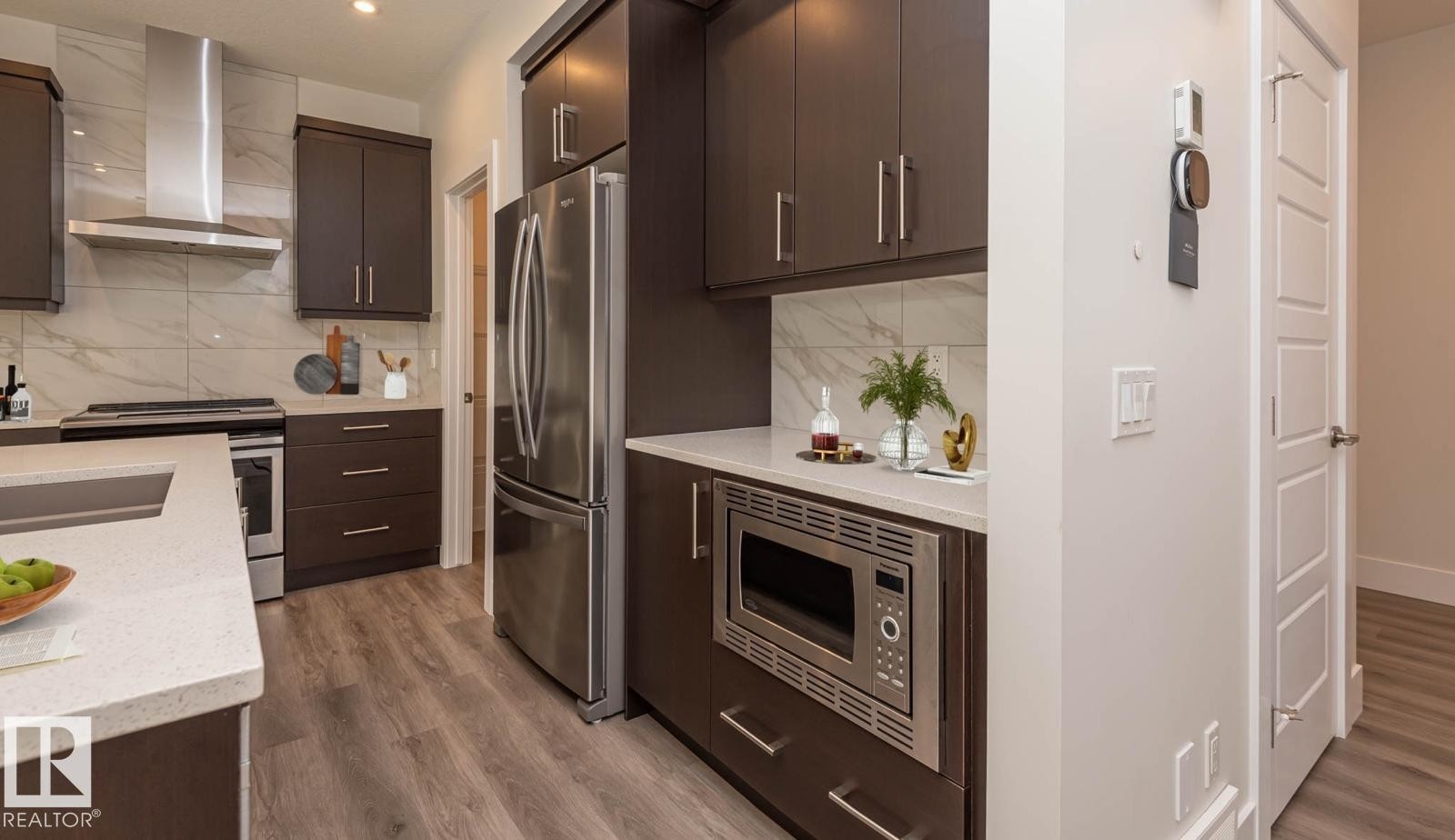 Contemporary kitchen featuring dark wood cabinetry, stainless steel appliances, and wood-finish flooring - 2635 Donaghey Crescent, Edmonton, AB
