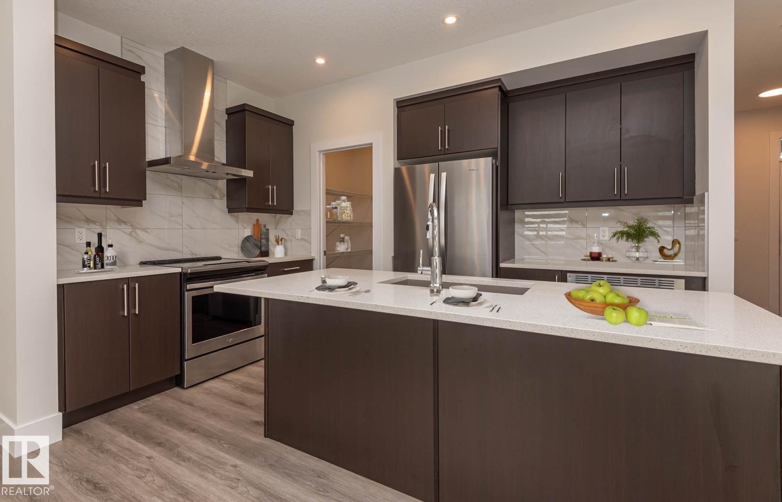 Modern kitchen featuring dark wood-finish cabinetry, stainless steel appliances, a white stone-finish island with an undermount sink, a tiled backsplash, and recessed lighting - 2635 Donaghey Crescent, Edmonton, AB