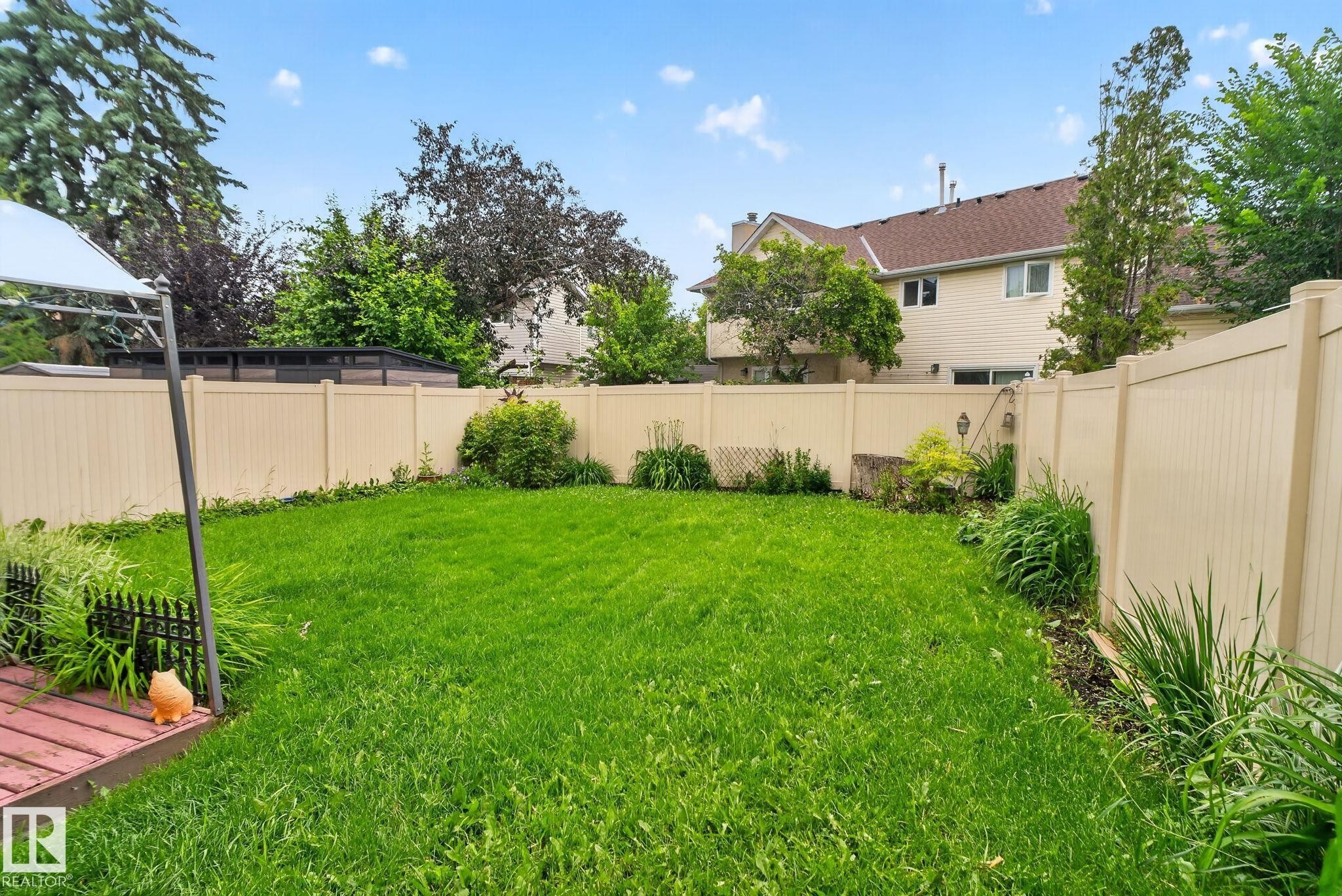 Expansive backyard featuring a lush lawn, perimeter fencing, mature trees, and a wooden deck - 9503 180A Street Nw, Edmonton, AB - Outdoor With Backyard