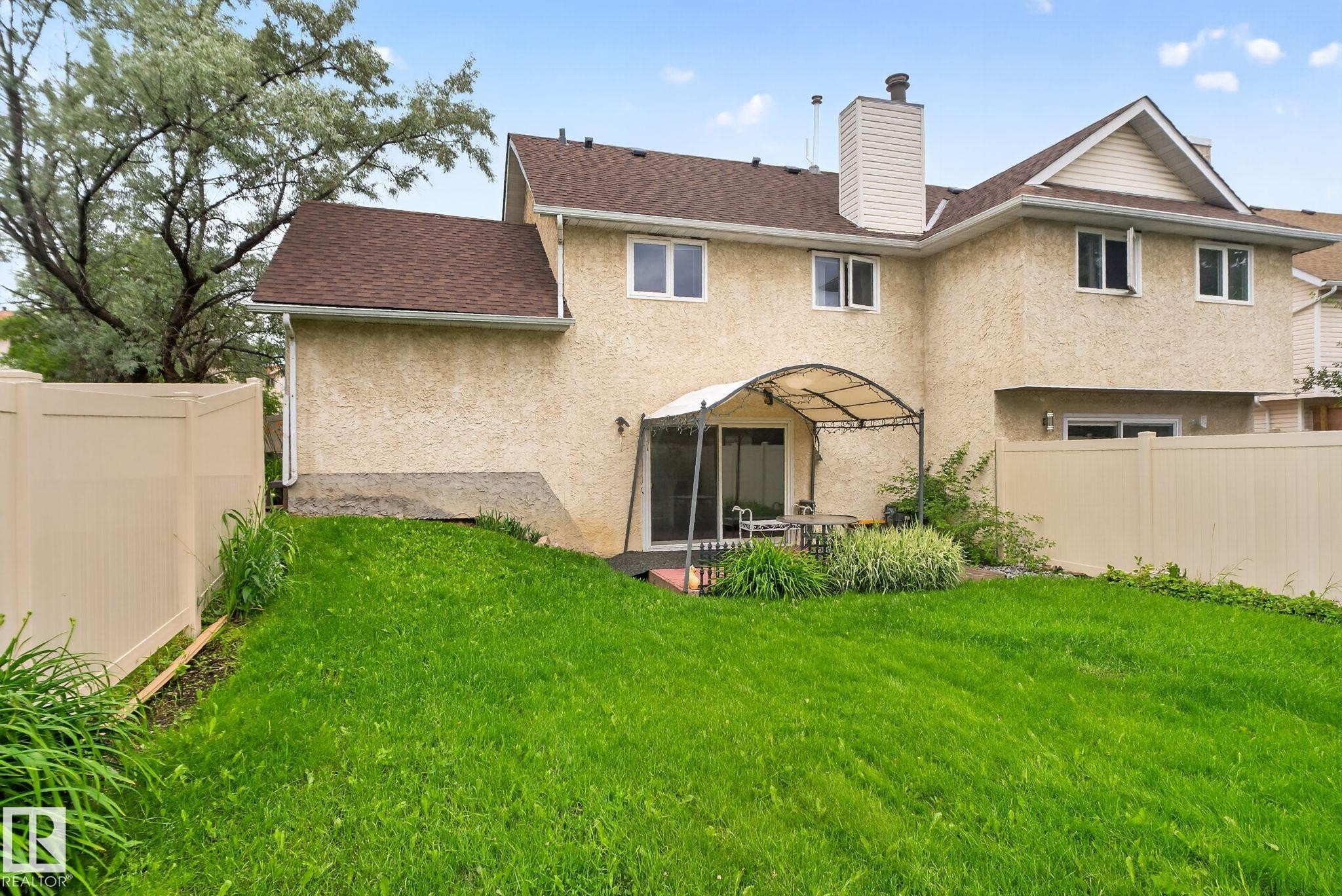 Expansive green lawn bordering a private patio area featuring a pergola - 9503 180A Street Nw, Edmonton, AB - Outdoor