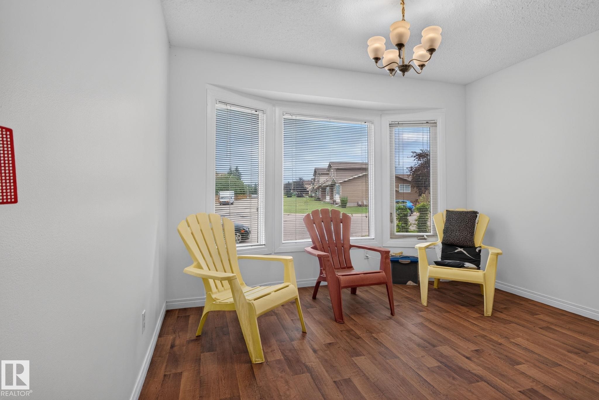 Room featuring wood-finish flooring, a multi-pane bay window with blinds, and a traditional chandelier light fixture - 9503 180A Street Nw, Edmonton, AB - Indoor