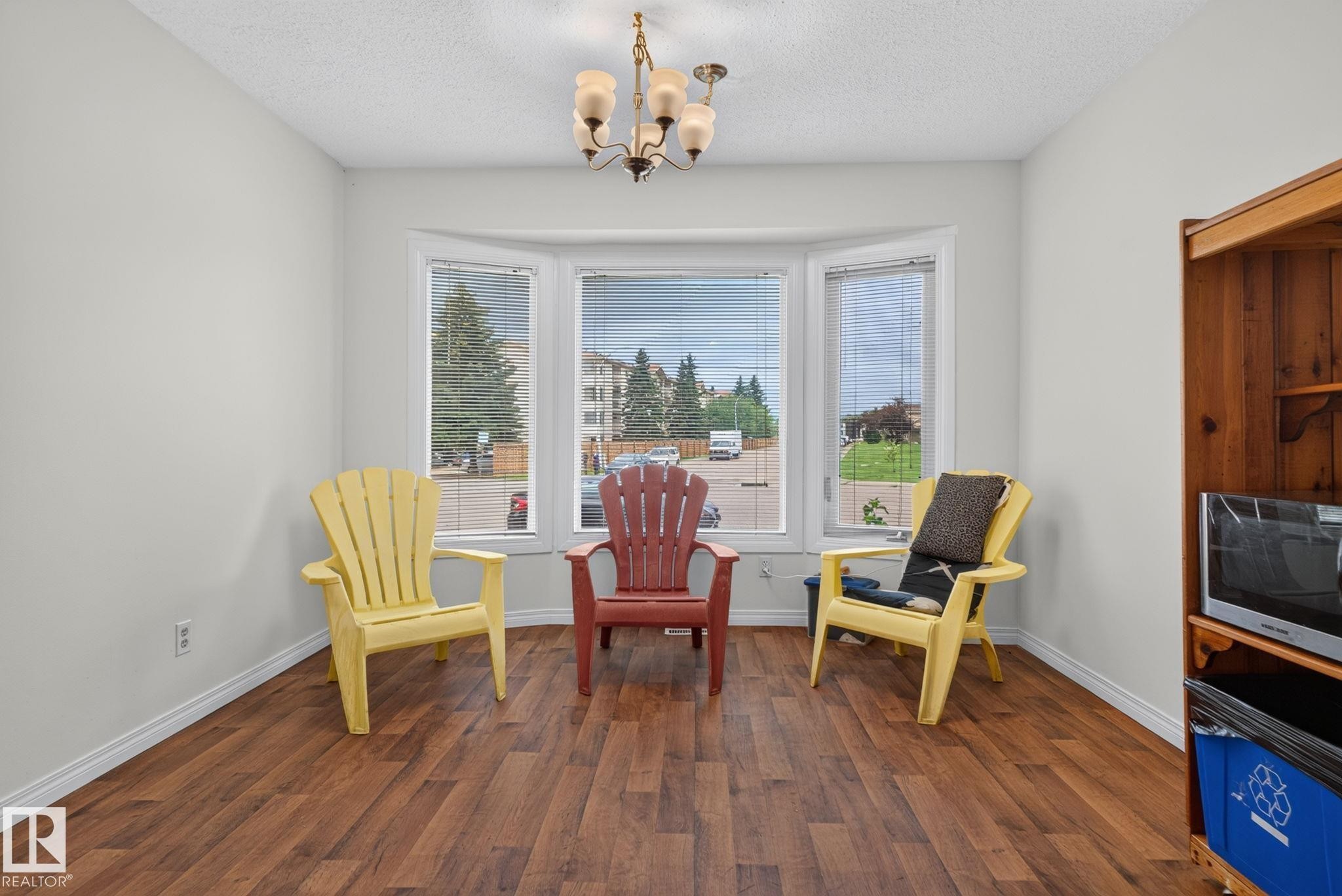 Bay window with three distinct panes, wood-finish flooring, white baseboards, and a chandelier light fixture - 9503 180A Street Nw, Edmonton, AB - Indoor