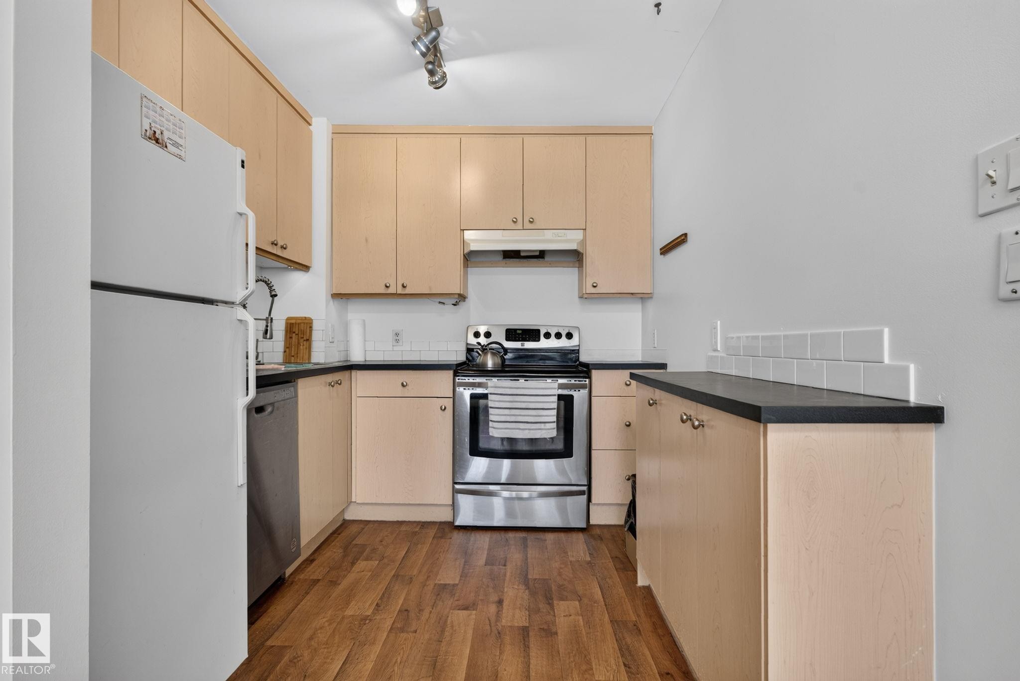 Compact kitchen featuring wood-finish flooring, light wood cabinetry, and contrasting dark countertops - 9503 180A Street Nw, Edmonton, AB - Indoor Photo Showing Kitchen With Stainless Steel Kitchen