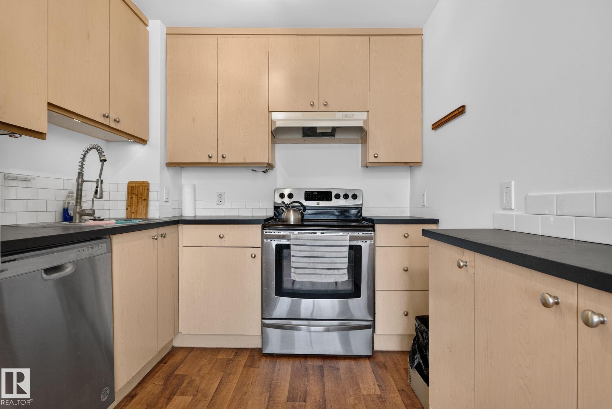 Kitchen featuring wood-finish cabinetry, stainless steel appliances, dark countertops, a white subway tile backsplash, and wood-finish flooring - 9503 180A Street Nw, Edmonton, AB - Indoor Photo Showing Kitchen With Stainless Steel Kitchen