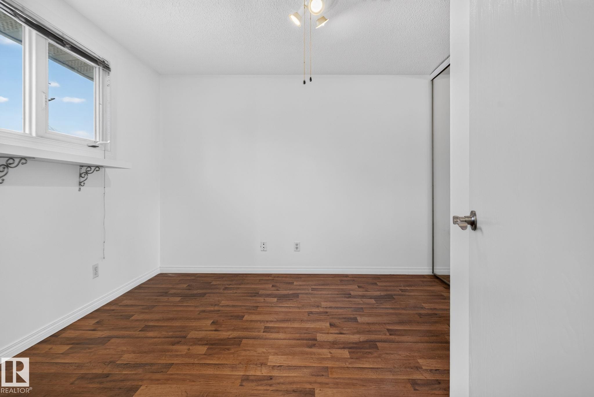 Room featuring wood-finish flooring, white baseboards, and a window with a shelf and decorative brackets - 9503 180A Street Nw, Edmonton, AB - Indoor Photo Showing Other Room