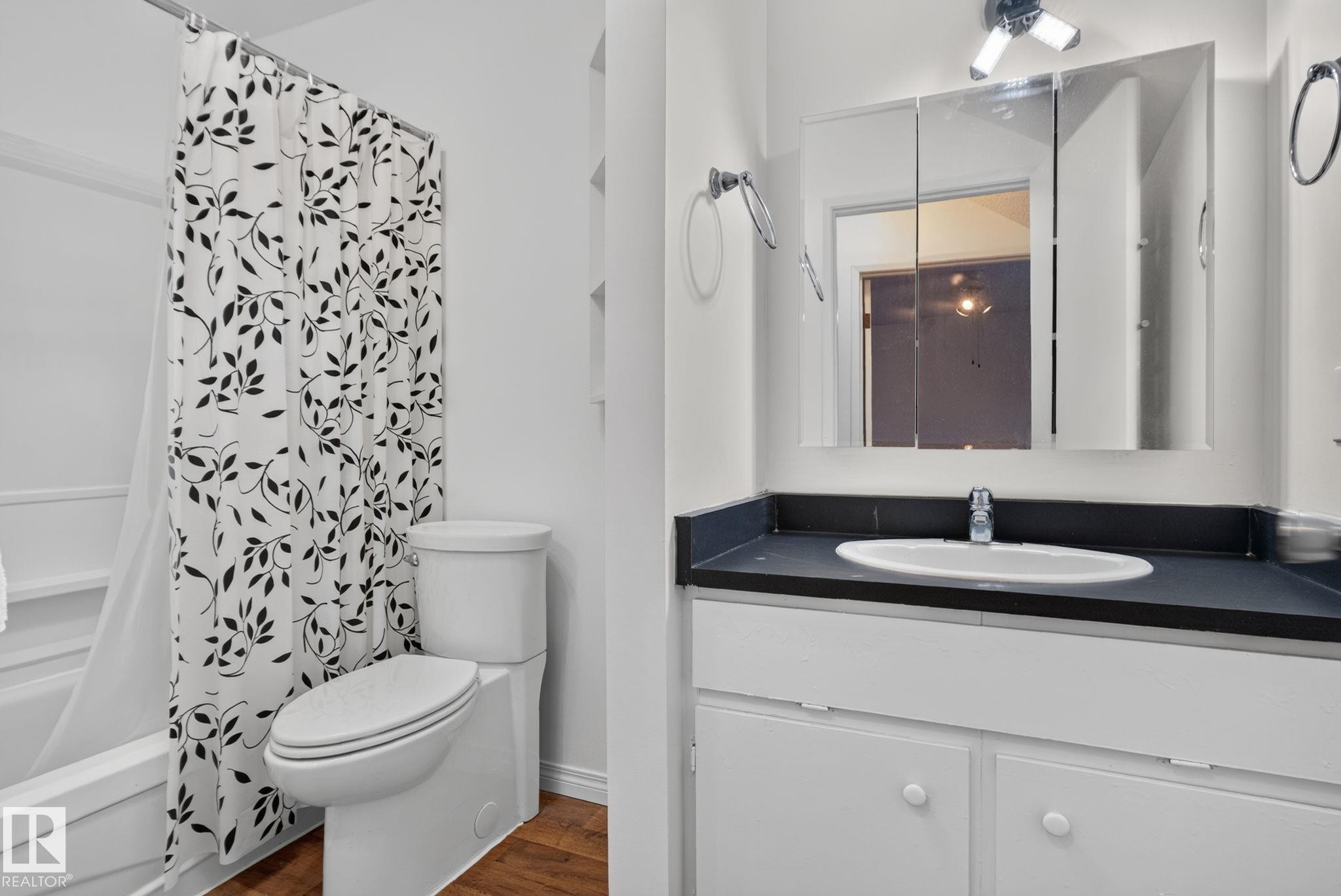 Bathroom featuring a white bathtub with shower, white toilet, and a vanity with a dark countertop and white cabinetry - 9503 180A Street Nw, Edmonton, AB - Indoor Photo Showing Bathroom