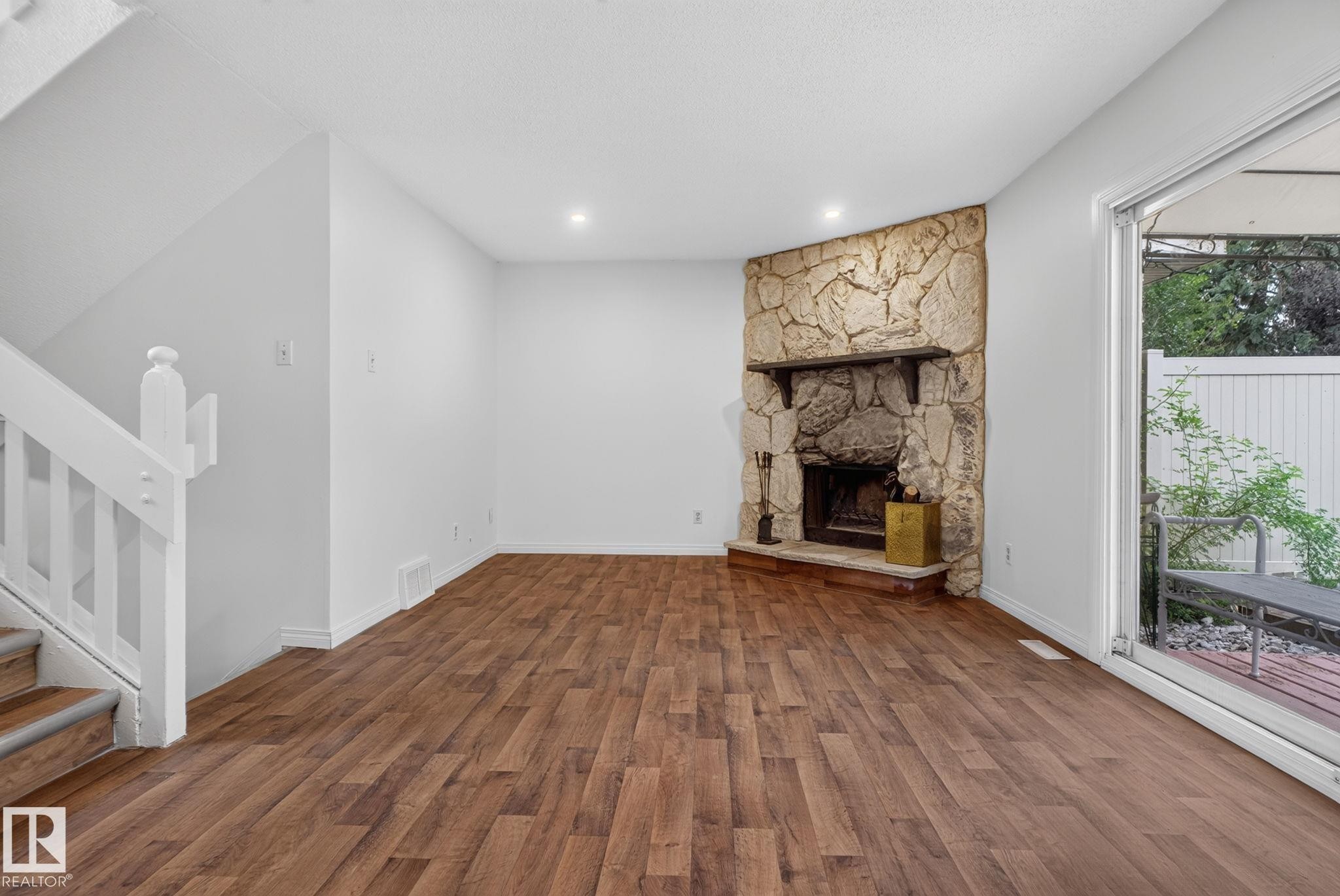 Stone-clad corner fireplace with a hearth, wood-finish flooring, and white painted walls - 9503 180A Street Nw, Edmonton, AB - Indoor With Fireplace
