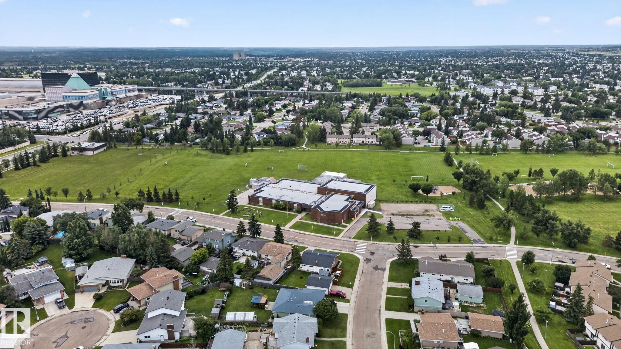Expansive aerial showing a residential neighborhood with detached homes, featuring significant green spaces and a public building - 9503 180A Street Nw, Edmonton, AB - Outdoor With View