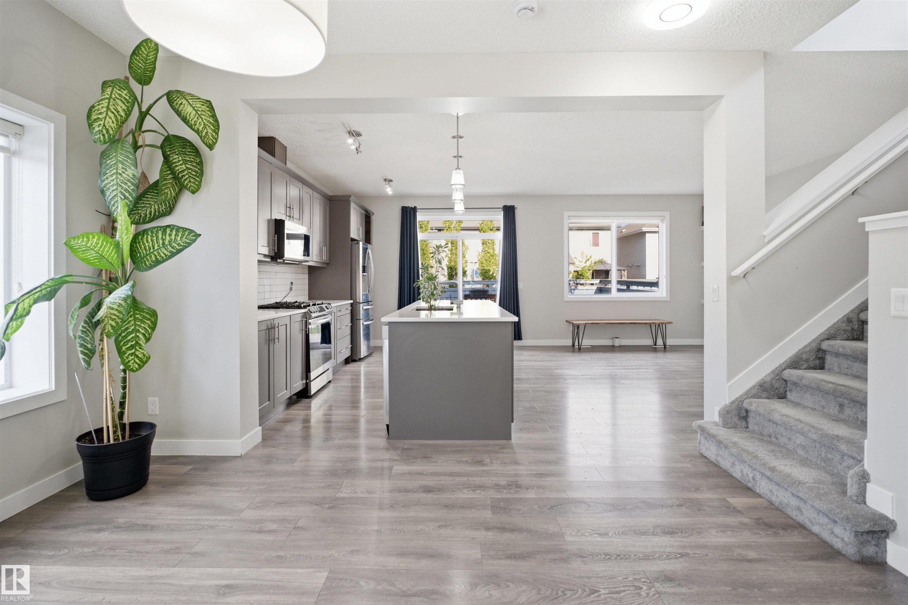 Open-concept main level featuring wood-finish flooring, a contemporary kitchen with stainless steel appliances, a central island with pendant lighting, and a carpeted staircase - 1234 Daniels Crescent, Edmonton, AB - Indoor