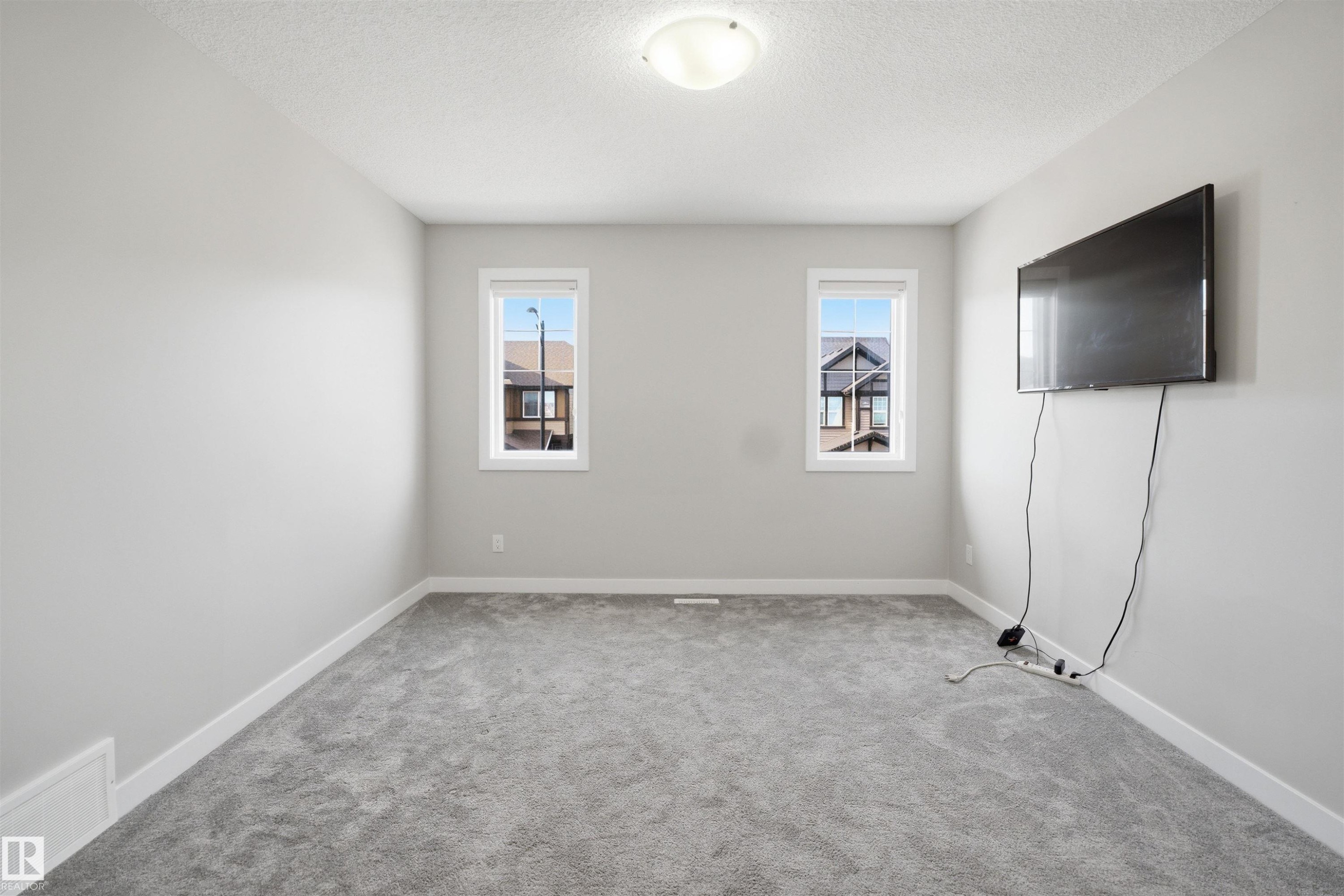 Carpeted interior space featuring light gray walls, two windows with white trim, and a ceiling-mounted light fixture - 1234 Daniels Crescent, Edmonton, AB - Indoor Photo Showing Other Room