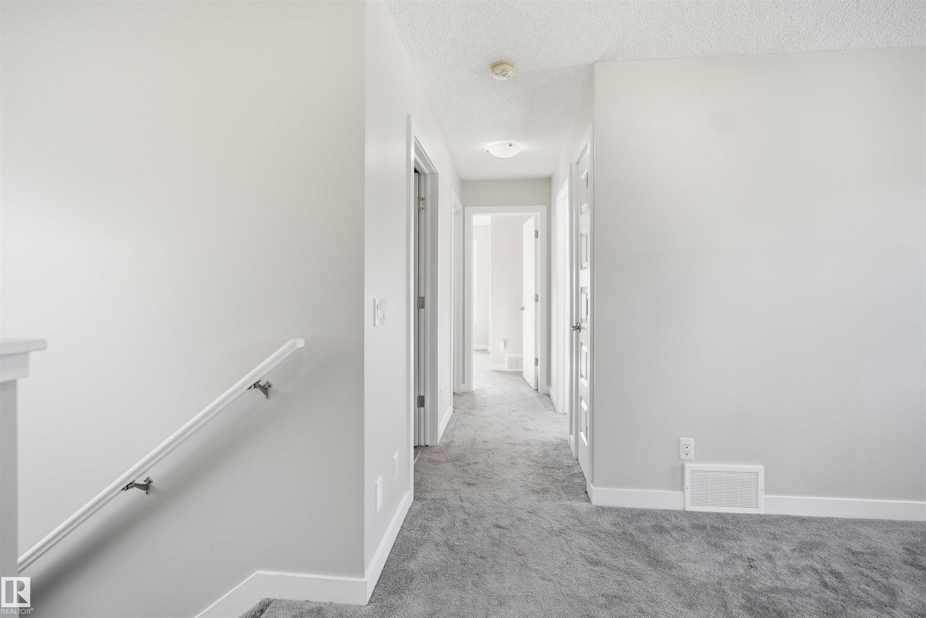 Interior hallway featuring light gray walls, gray carpet flooring, white baseboards, and white doors - 1234 Daniels Crescent, Edmonton, AB - Indoor Photo Showing Other Room