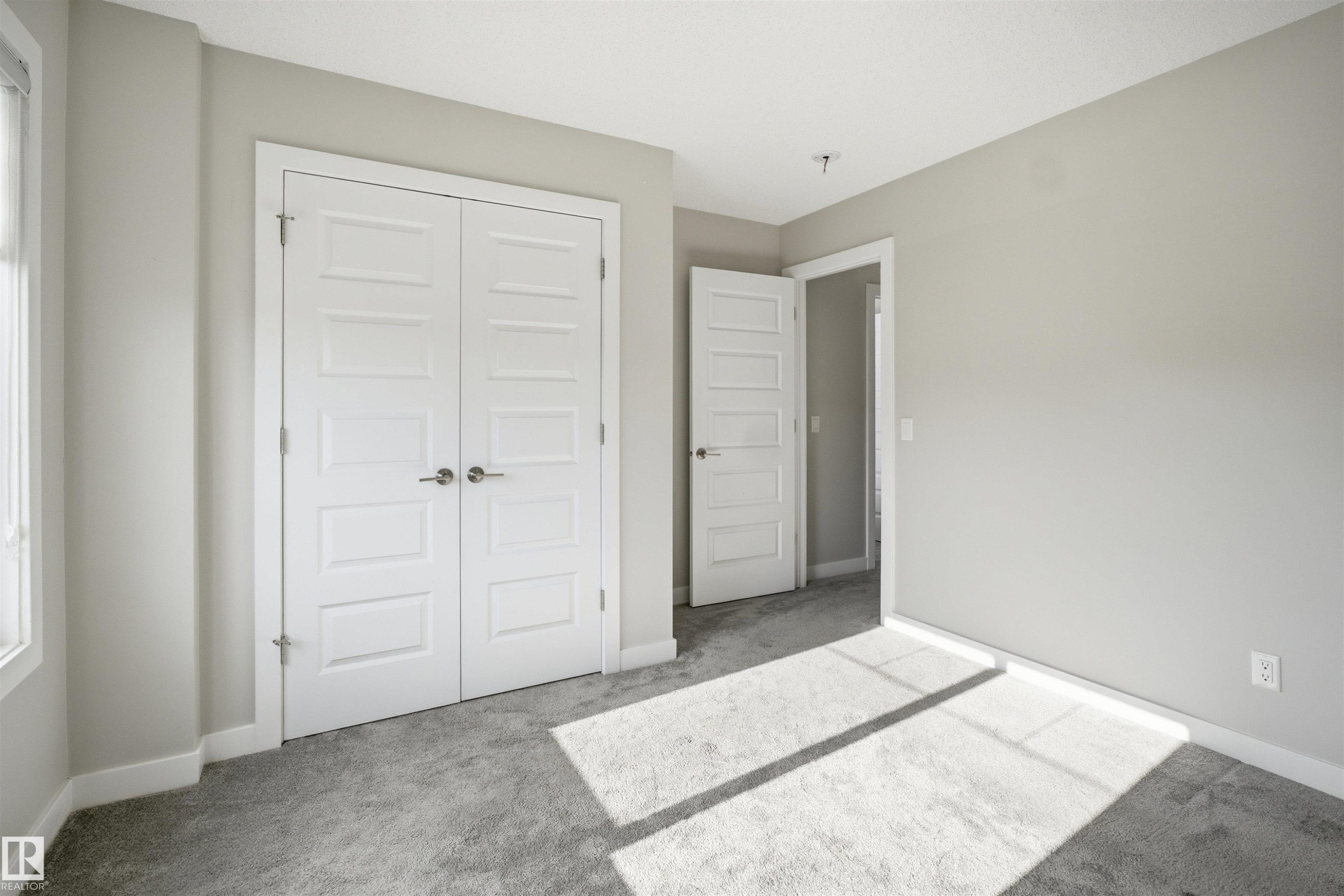 Light gray wall paint with white trim, gray carpet, and two white panel doors with brushed nickel hardware - 1234 Daniels Crescent, Edmonton, AB - Indoor Photo Showing Other Room