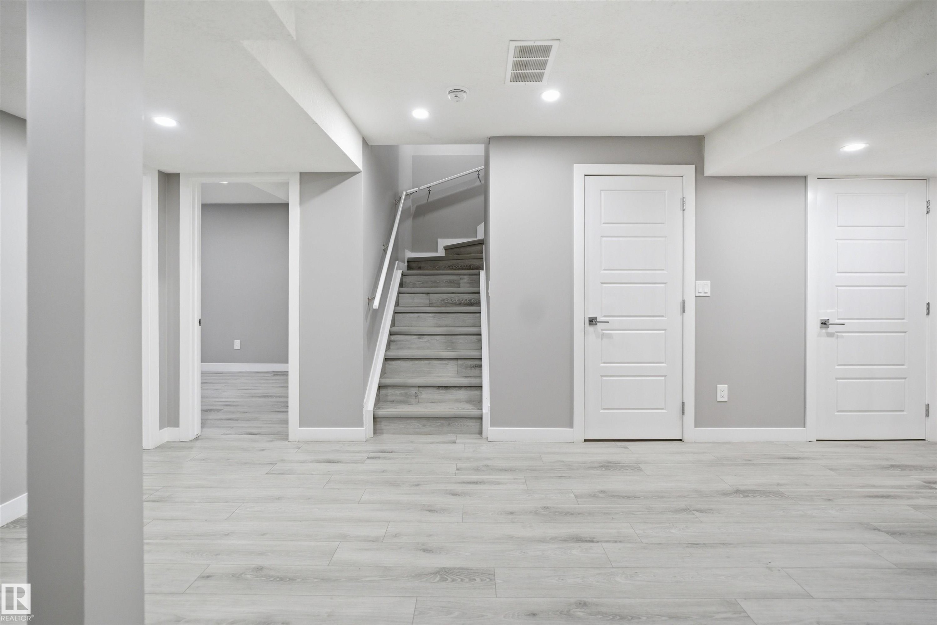 Versatile lower level featuring light wood-finish flooring, recessed lighting, and a staircase with a glass and metal railing - 1234 Daniels Crescent, Edmonton, AB - Indoor Photo Showing Other Room