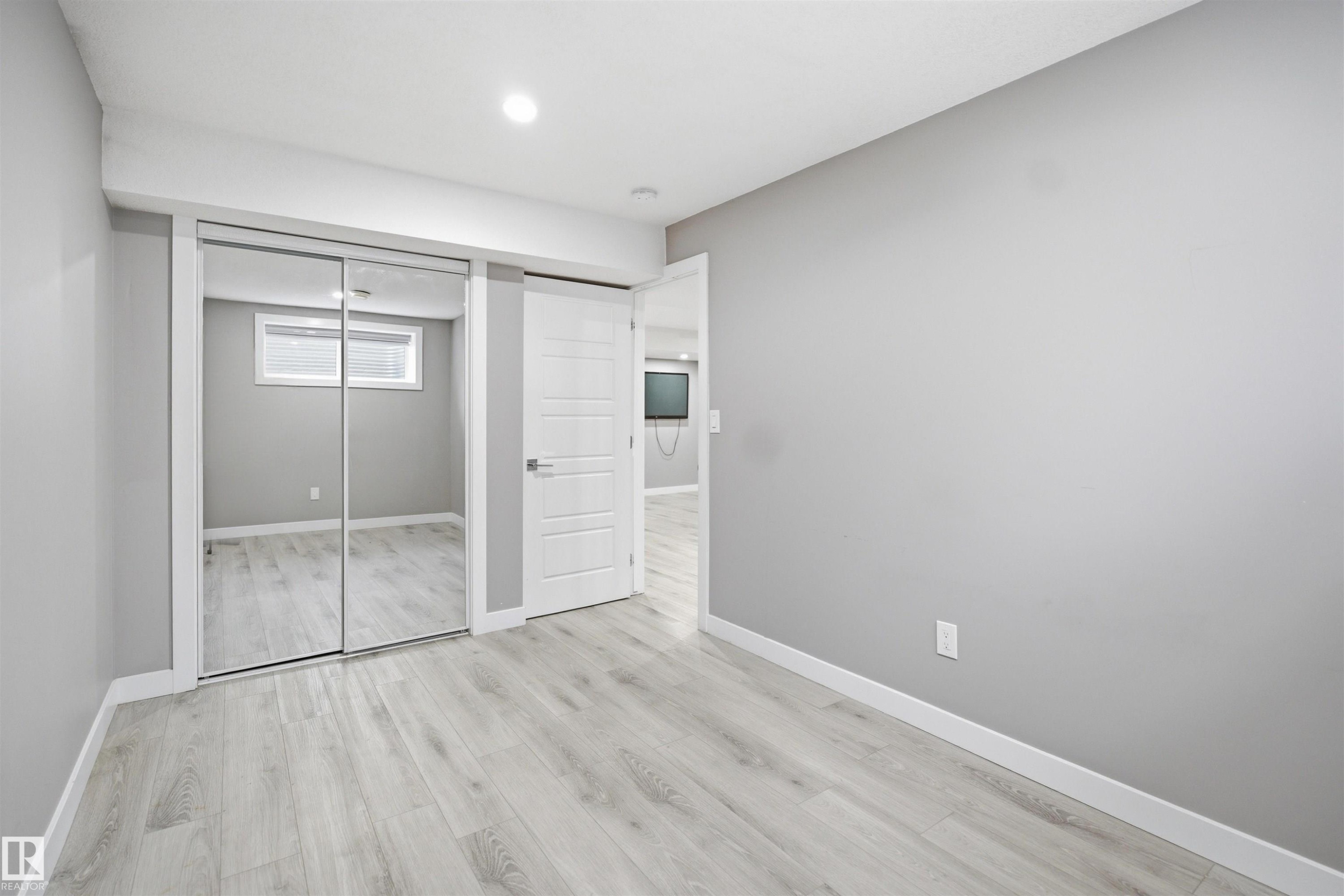 Light gray walls complement wood-finish flooring in this room featuring a mirrored closet with sliding doors and a white paneled door - 1234 Daniels Crescent, Edmonton, AB - Indoor Photo Showing Other Room