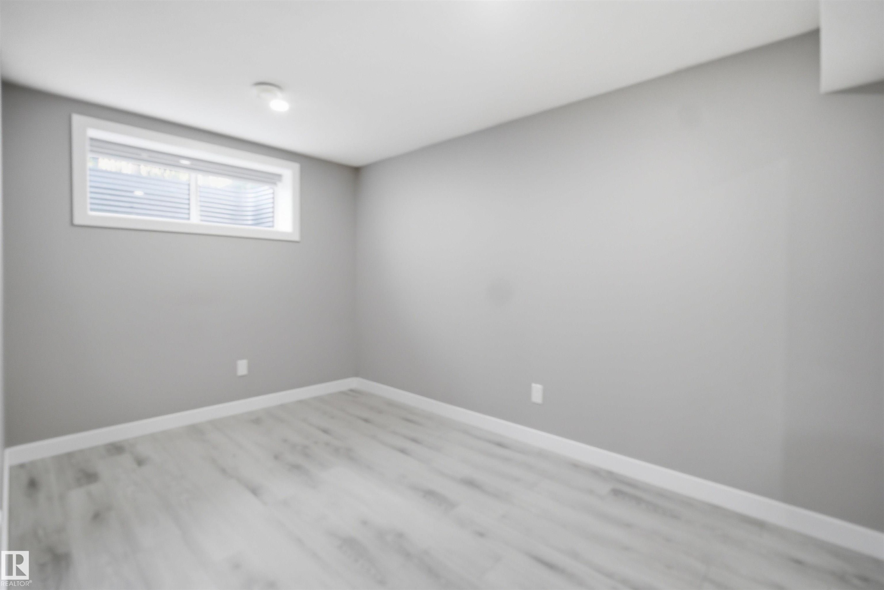 Light gray wood-finish flooring complements the matching wall color and white baseboards - 1234 Daniels Crescent, Edmonton, AB - Indoor Photo Showing Other Room