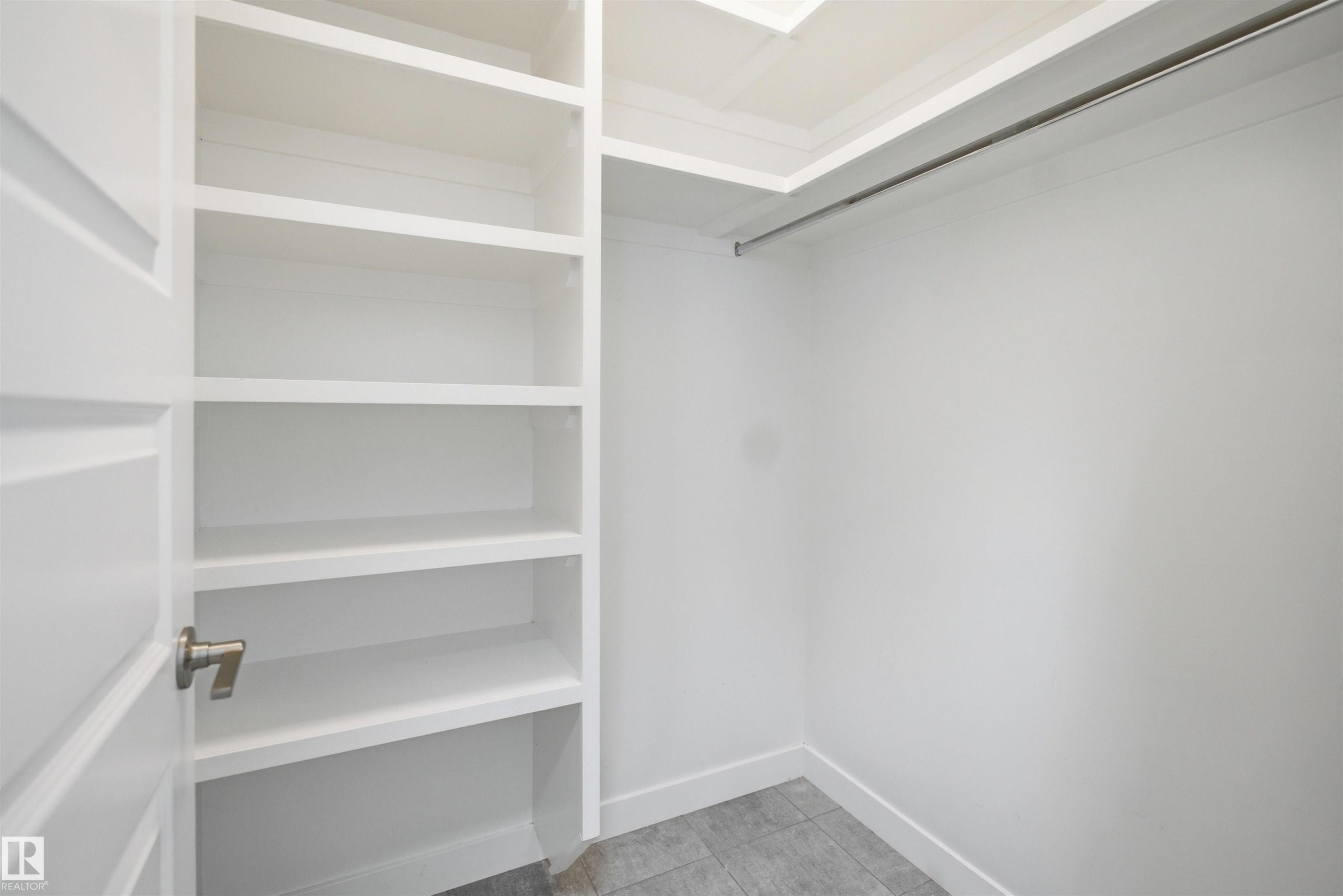 Built-in closet system featuring white shelving, a full-width hanging rod, and grey tile flooring - 1234 Daniels Crescent, Edmonton, AB - Indoor With Storage