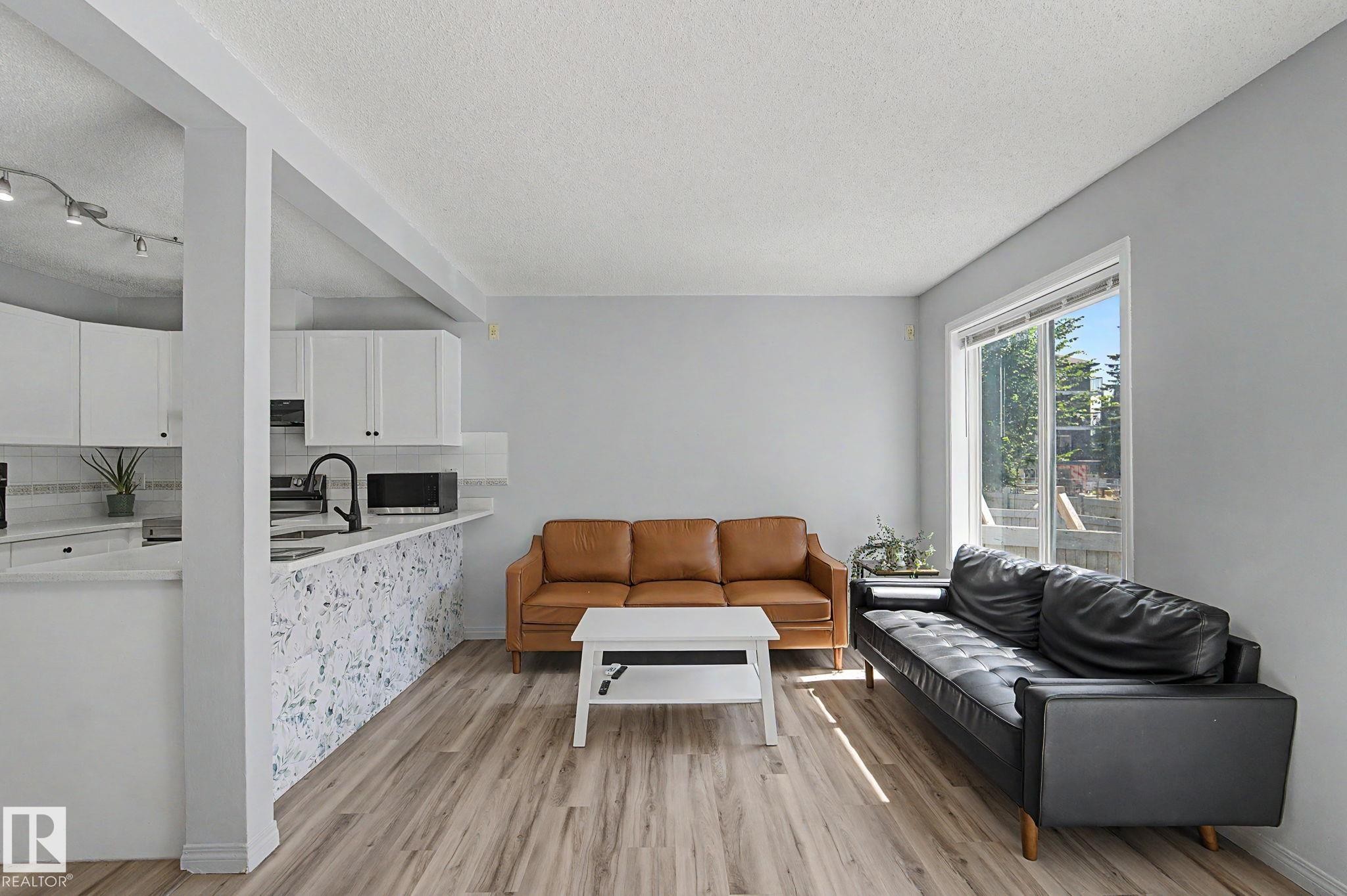 Open concept living area featuring wood-finish flooring, a large window, and light gray walls - 5 14603 Miller Boulevard, Edmonton, AB