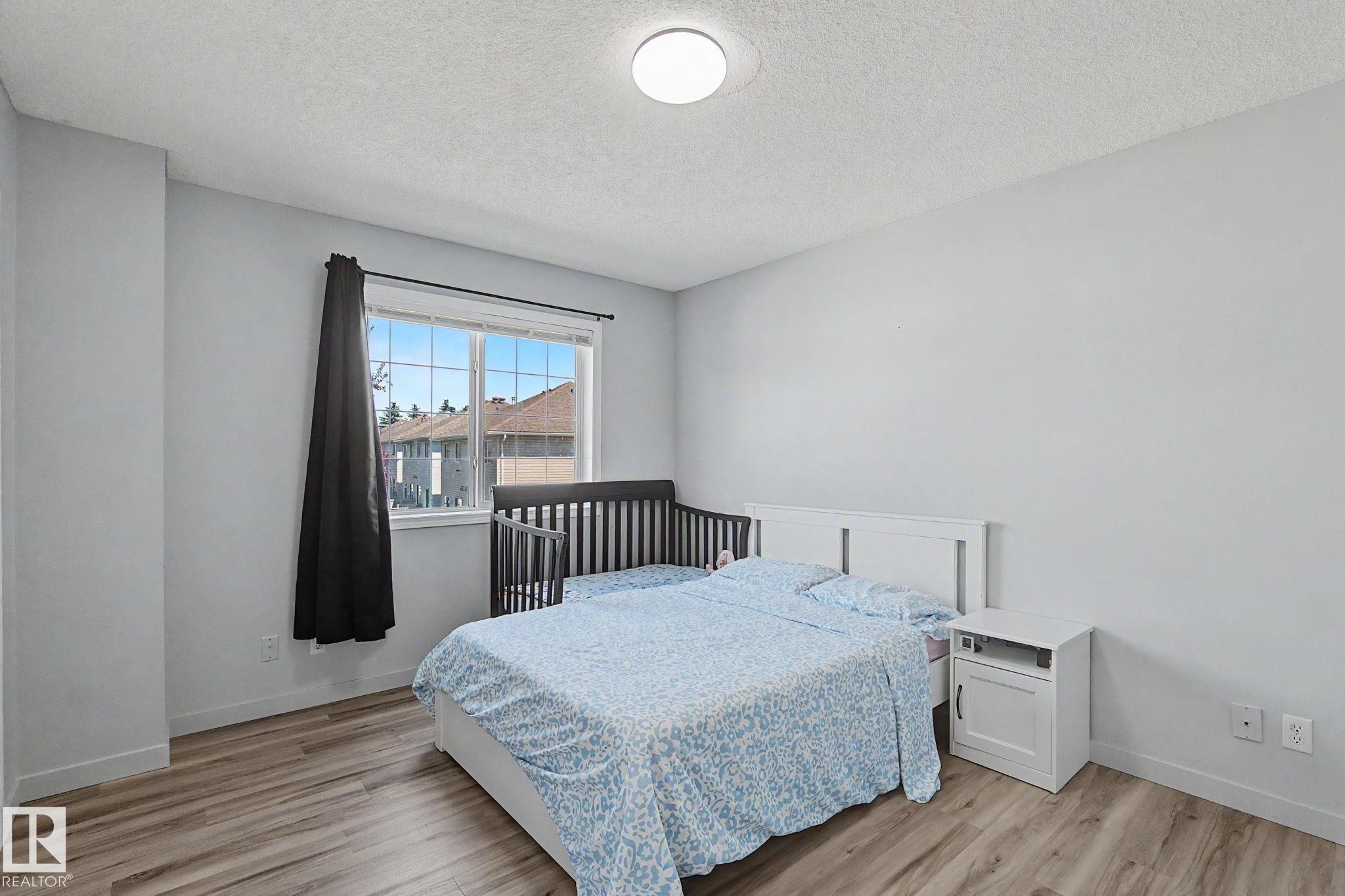 Bedroom featuring wood-finish flooring, a contemporary ceiling light fixture, and a large window - 5 14603 Miller Boulevard, Edmonton, AB
