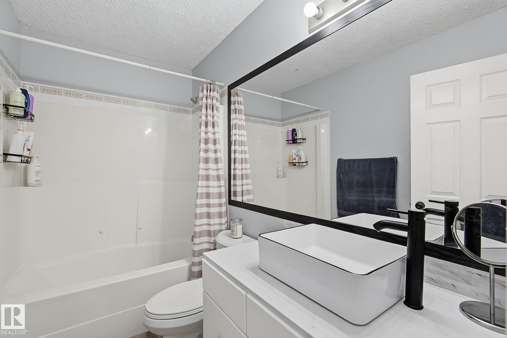 Bathroom featuring a white vanity with an integrated vessel sink, black faucet, and a large wall-mounted mirror with black trim - 5 14603 Miller Boulevard, Edmonton, AB
