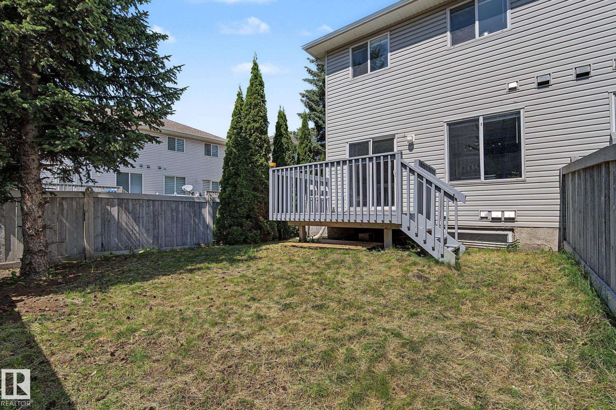 Private backyard featuring a wooden deck with railing, stairs, and access to the home - 5 14603 Miller Boulevard, Edmonton, AB